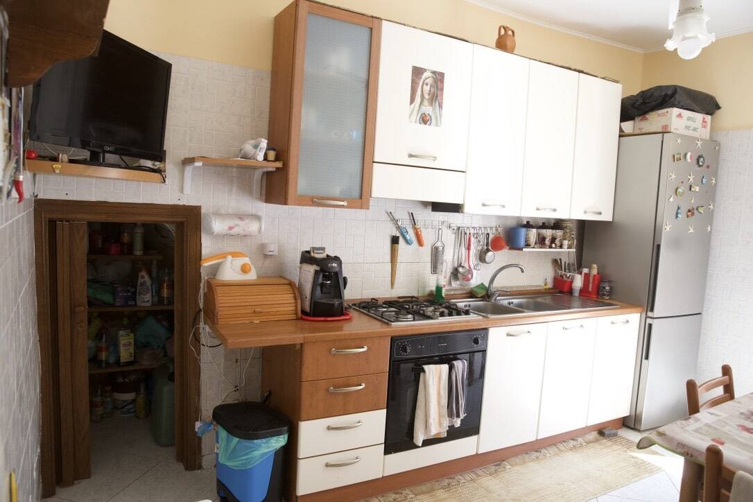 Scaffale cucina in legno con ripiani aperti, utensili da cucina, microonde e frigorifero in un ambiente domestico accogliente e funzionale, ideale per la vita quotidiana.