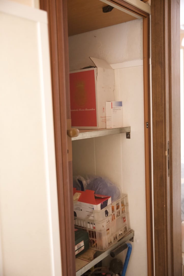 Stanza di negozio o ripostiglio con scaffali e scatole di imballaggi, spazio di stoccaggio per articoli vari e materiali di lavoro, all’interno di un ambiente con pareti bianche e struttura in legno.