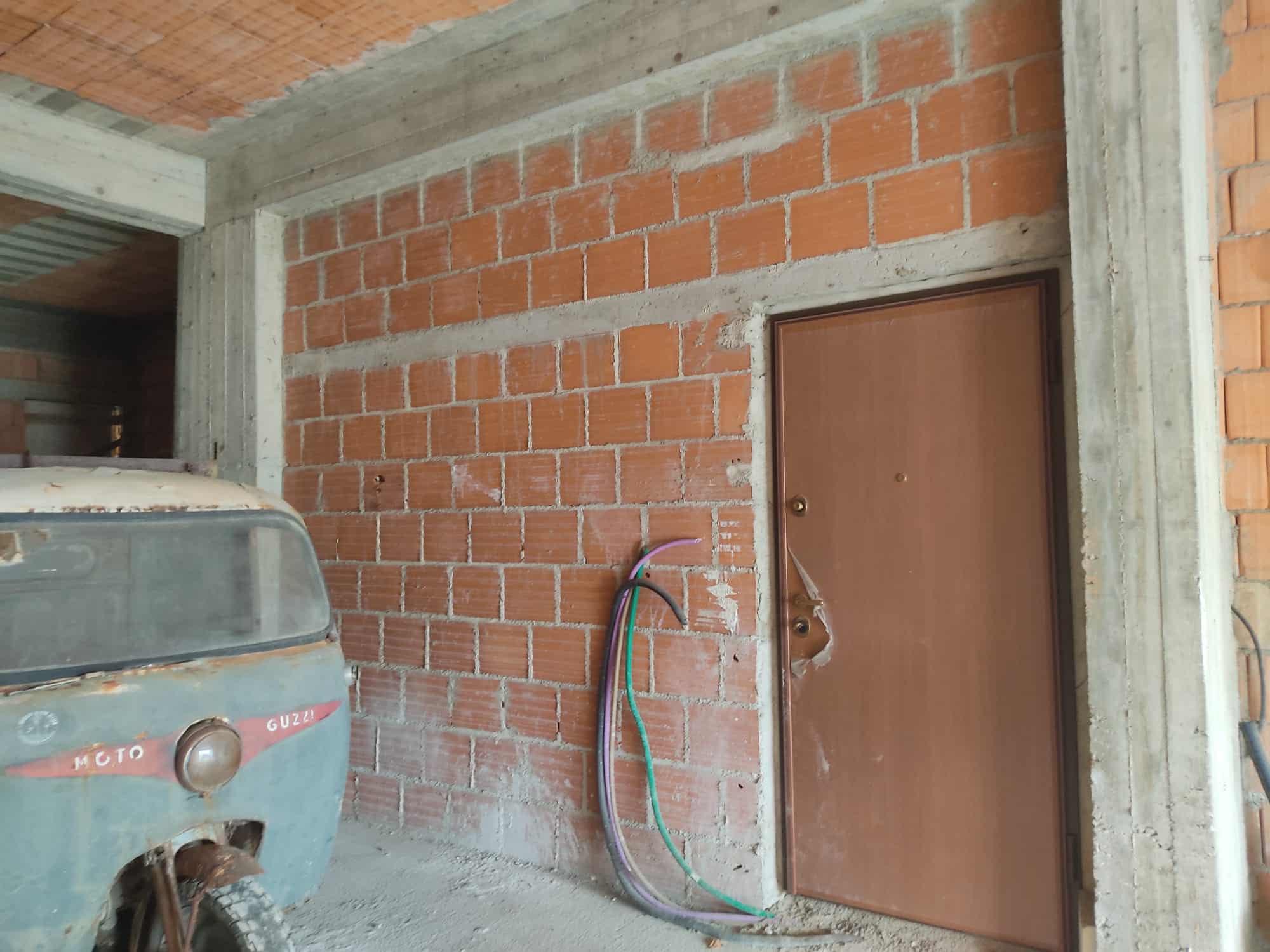Moto Guzzi, moto d'epoca in fase di restauro o conservazione, in un contesto di costruzione o ristrutturazione di un edificio, con pareti in laterizio e canali di distribuzione dell'acqua sullo sfondo.
