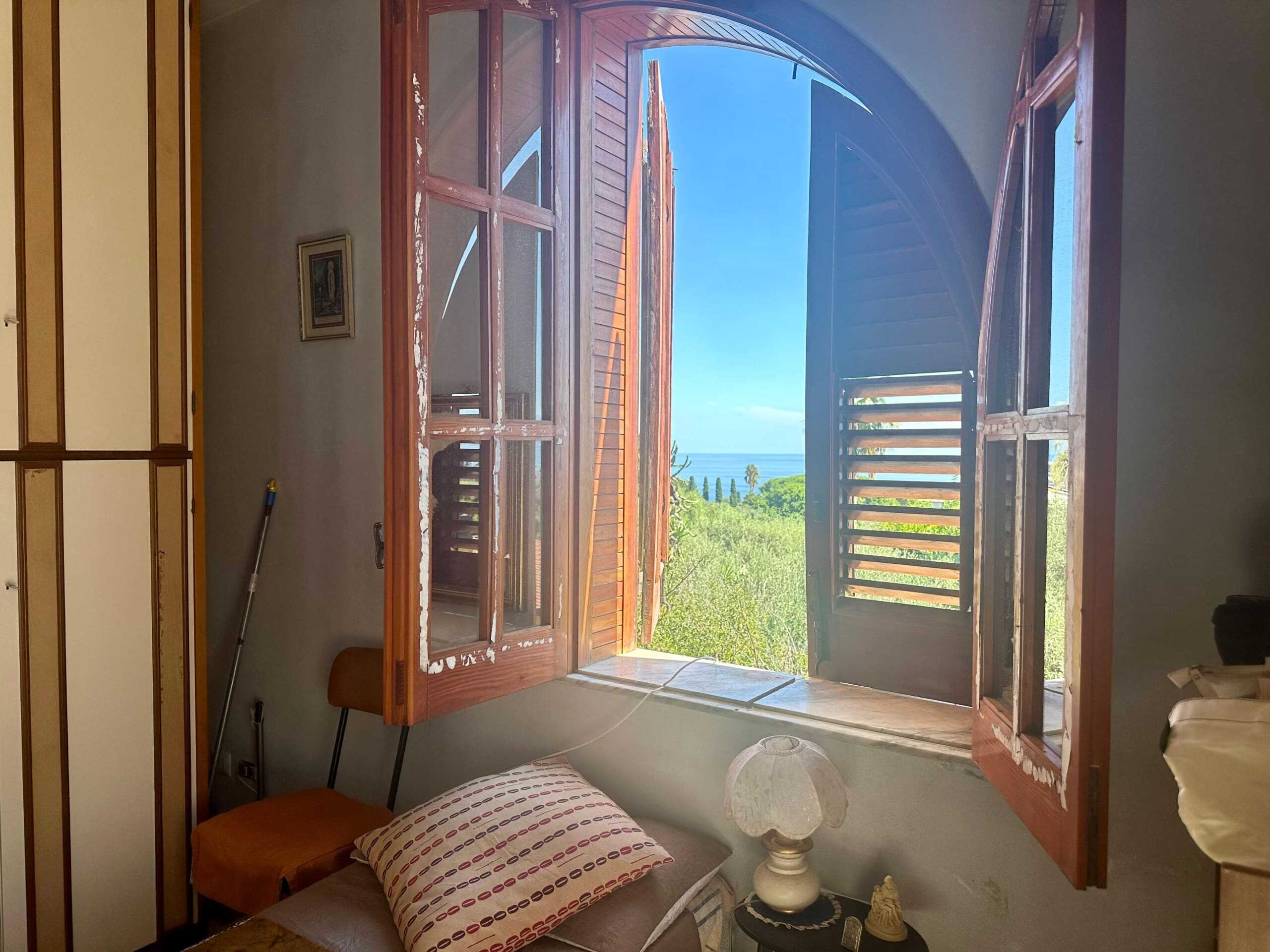 Finestra in legno con vista mare, interni di casa in stile rustico, vista panoramica sul paesaggio verde e il mare, arredo classico, luce naturale, atmosfera accogliente.