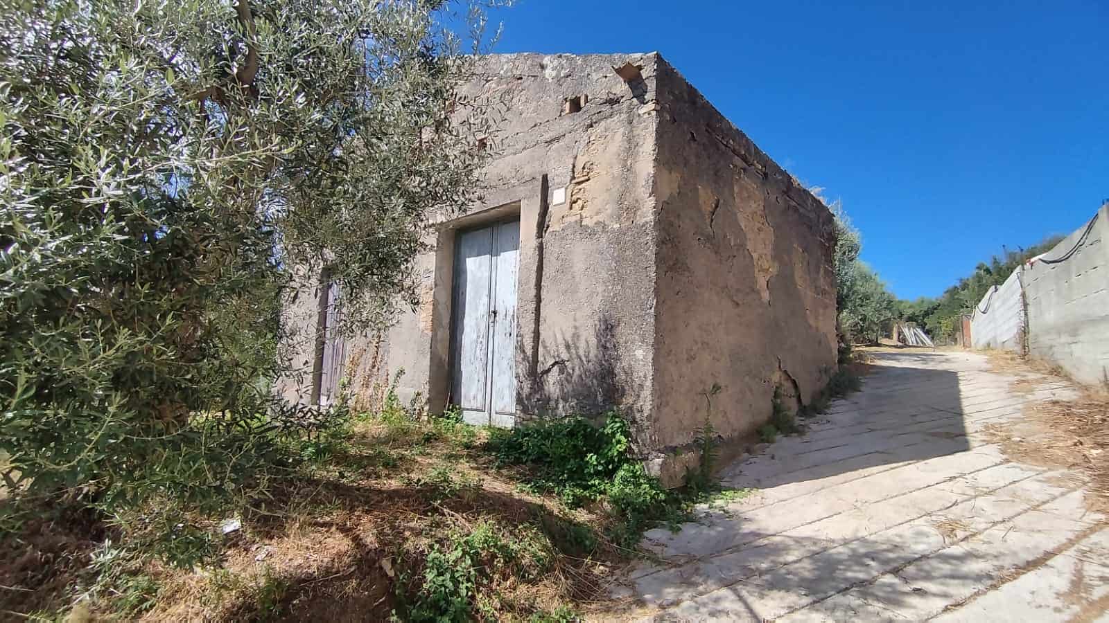 Vecchio casolare in pietra con porta in legno, situato in campagna, circondato da alberi e natura, ideale per ristrutturazione e sviluppo immobiliare, panorama rurale e tranquillo.