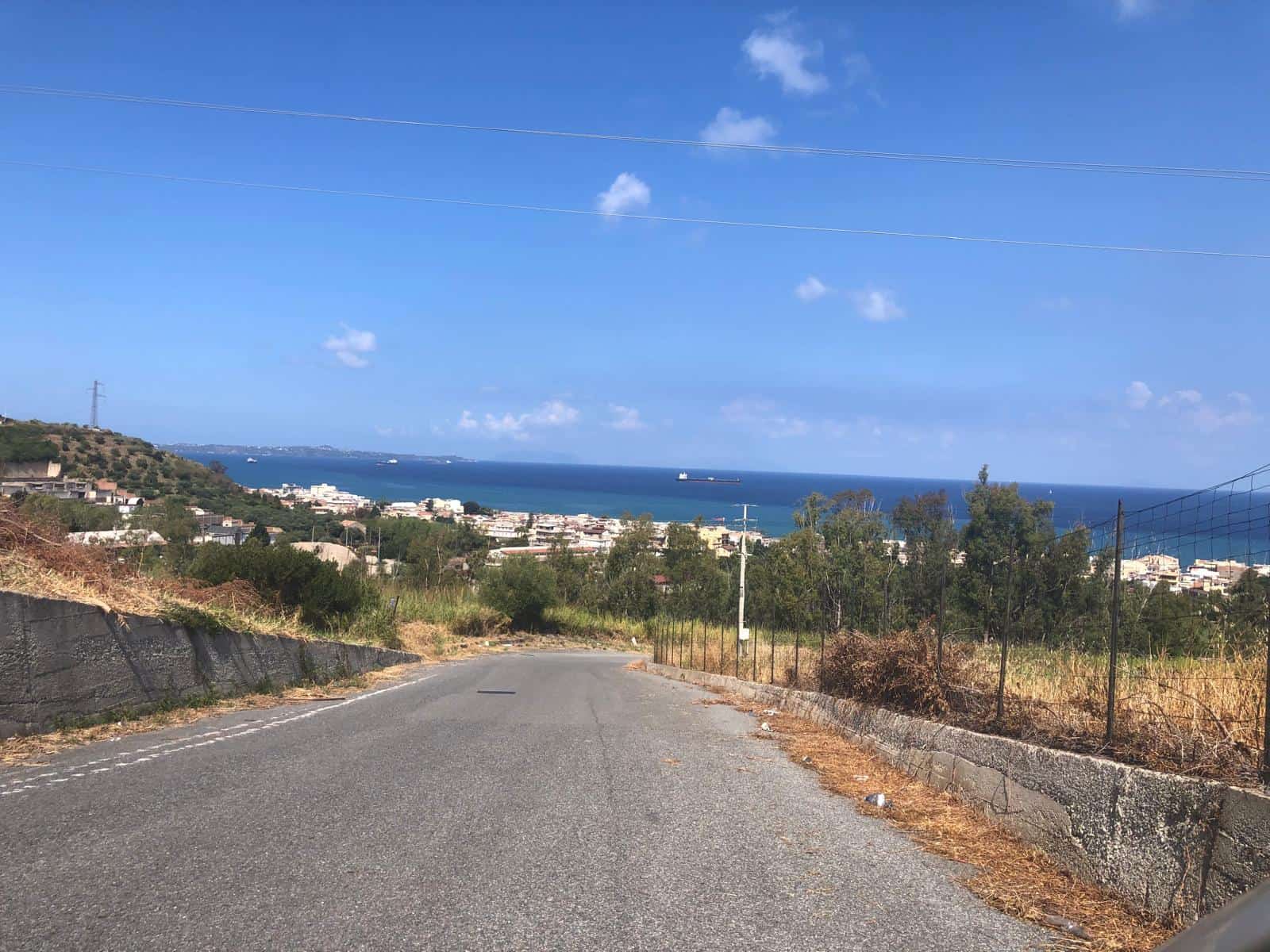 Vista panoramica sul mare e sulla costa dalla strada in zona residenziale, con cielo sereno e dolci colline, ideale per immobili con vista mare e natura in Sicilia.