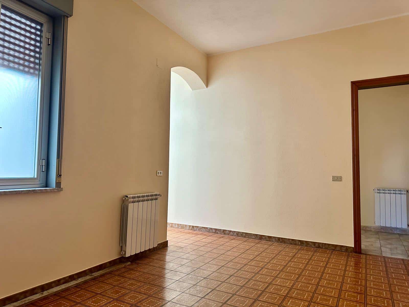 Finestra e pareti beige in un appartamento luminoso con riscaldamento a radiatori, pavimenti in ceramica con motivo geometrico, ingresso a sala da pranzo o soggiorno.