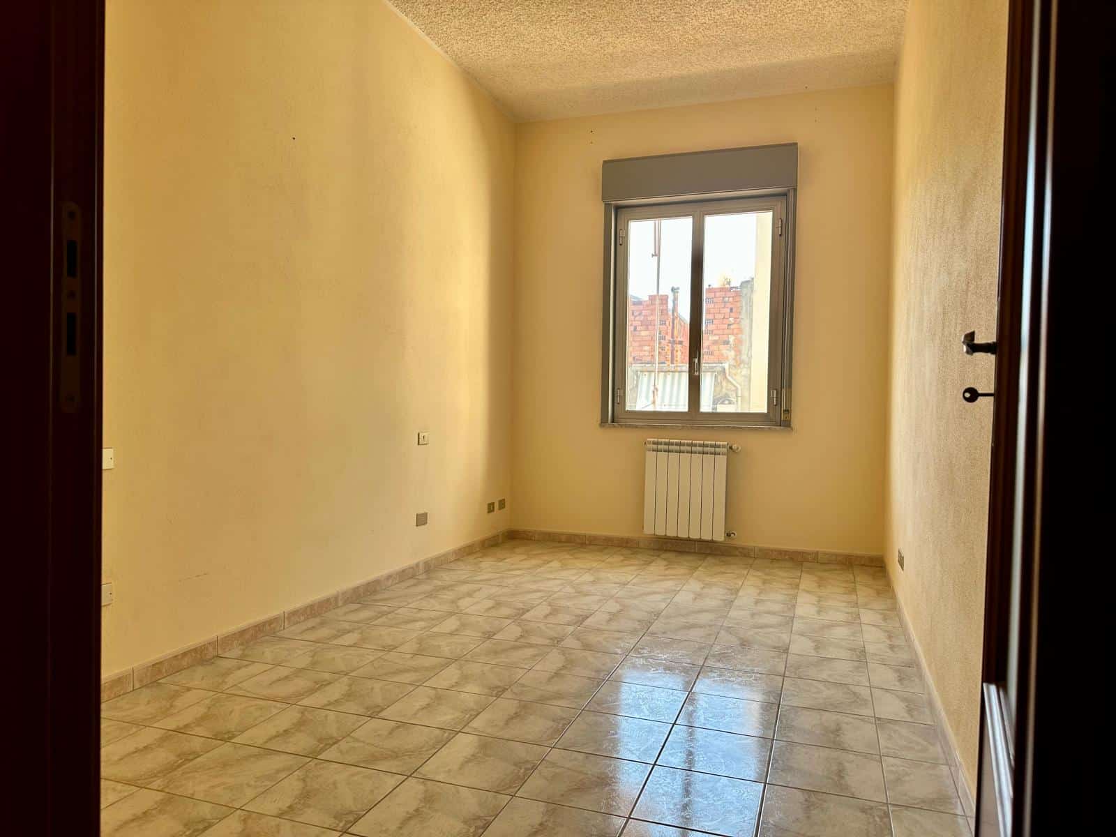 Ampio appartamento vuoto con pareti gialle, grande finestra e bagno radiante, ideale per affitti o ristrutturazioni, a pochi passi dai servizi principali in zona residenziale.