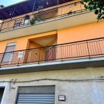 Balcone di appartamento con ringhiera in ferro nero, decorativa, e vasi con piante e fiori, facciata di edificio residenziale con pareti colorate in arancione e beige, finestre con tapparelle.