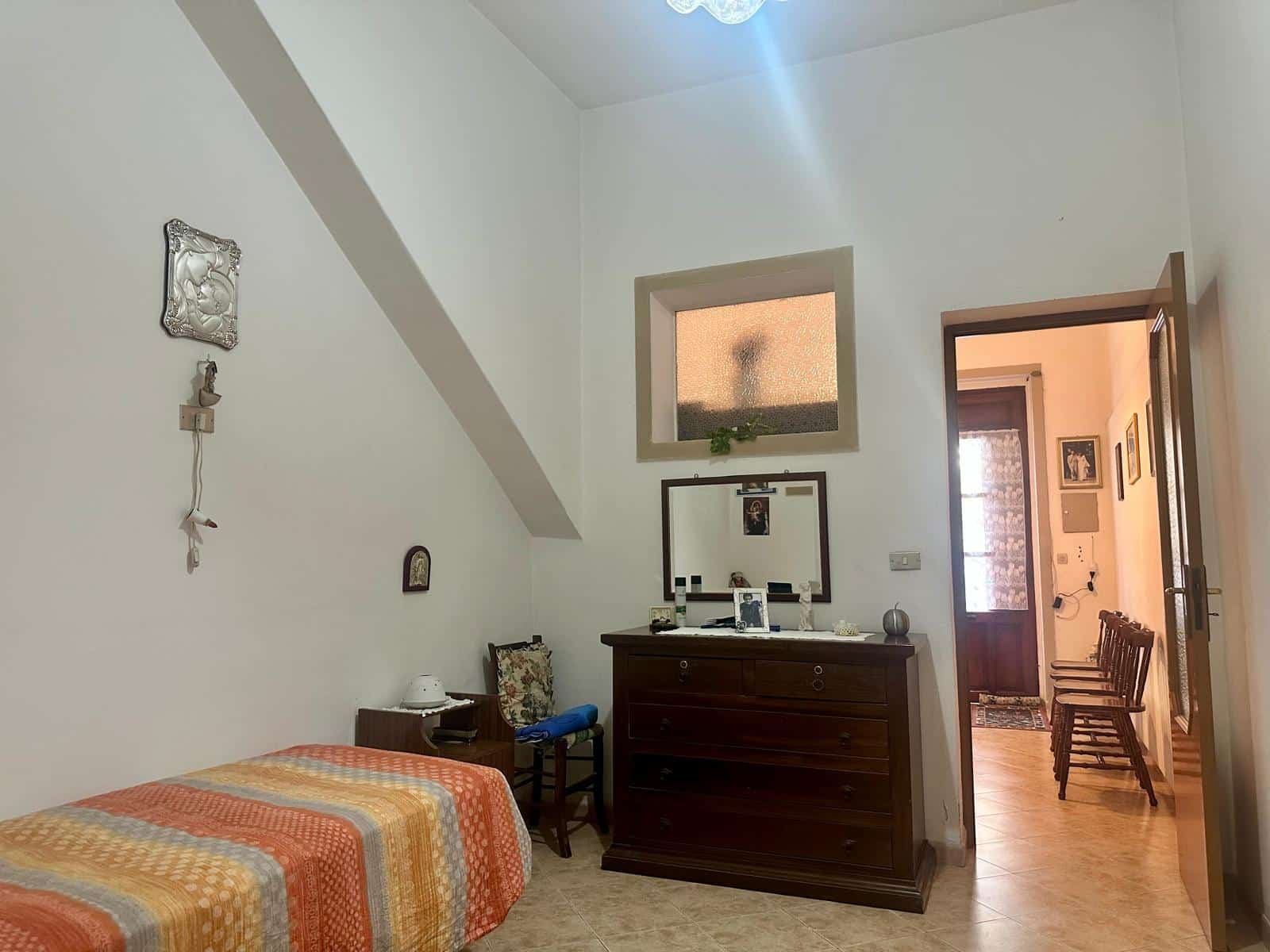 Letto singolo in camera con arredi classici, pareti bianche e bagno adiacente, ambiente luminoso e accogliente, ideale per soluzioni abitative convenienti e funzionali, stile tradizionale.