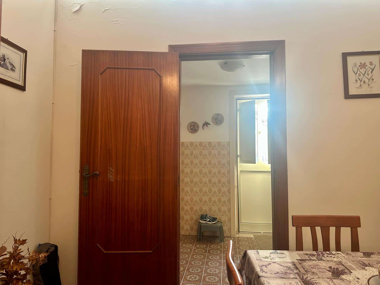 Porta in legno di una casa di famiglia, vista dal soggiorno con pareti decorate e un tavolo apparecchiato, ambiente luminoso con accesso alla cucina attraverso una porta finestra.