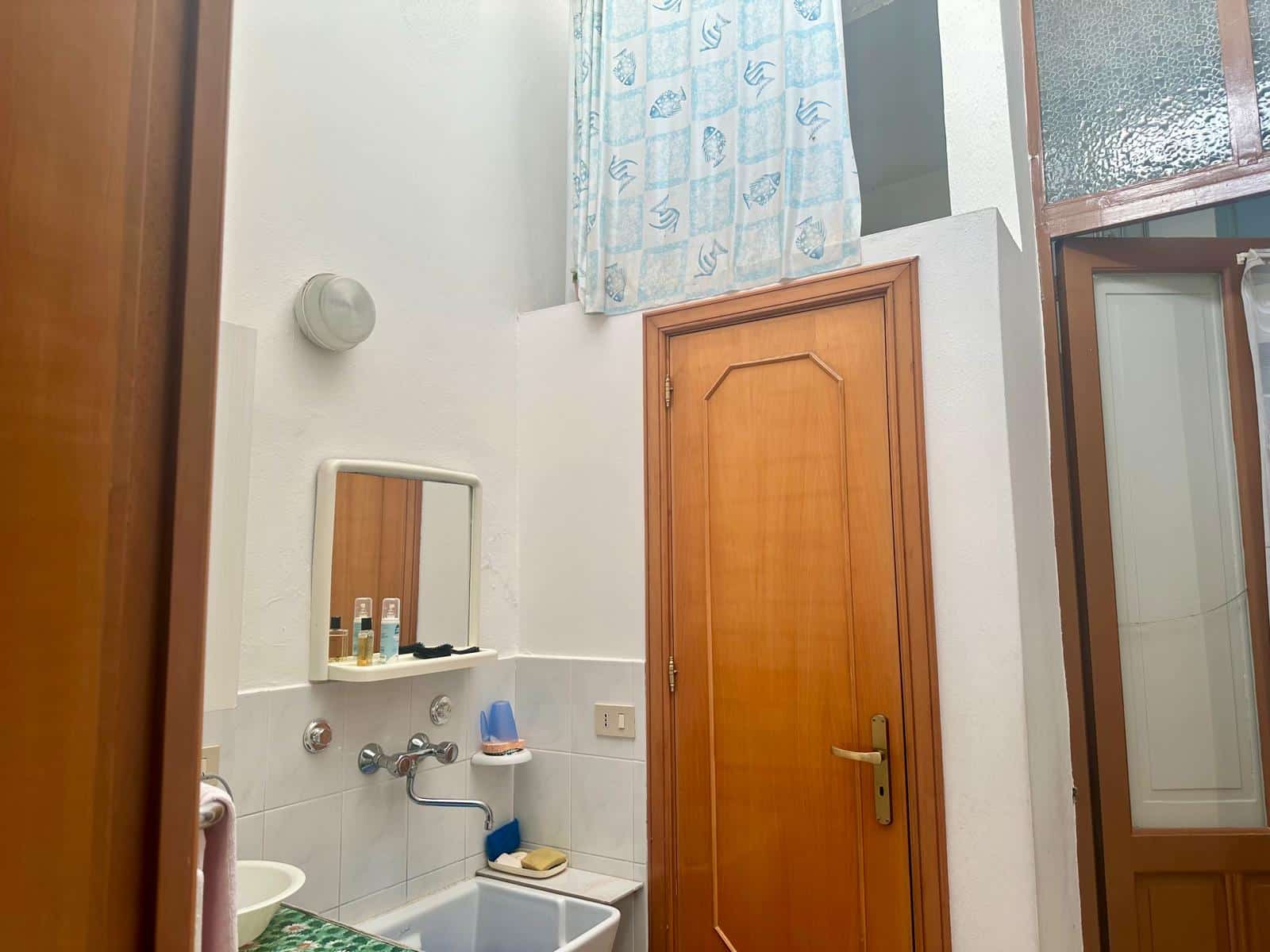 Lavanderia con mobile in legno, sgabello, specchio, ripostiglio, stendibiancheria e dettagli di arredamento in stile classico, ideale per case in vendita o affitto.