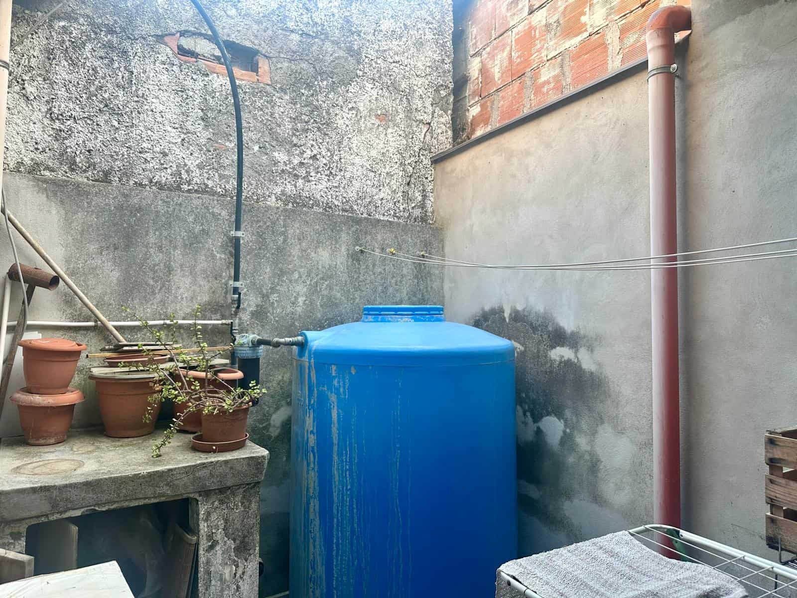 Serbatoio acqua blu in un'area esterna di una proprietà immobiliare, con pareti in cemento e mattoni.