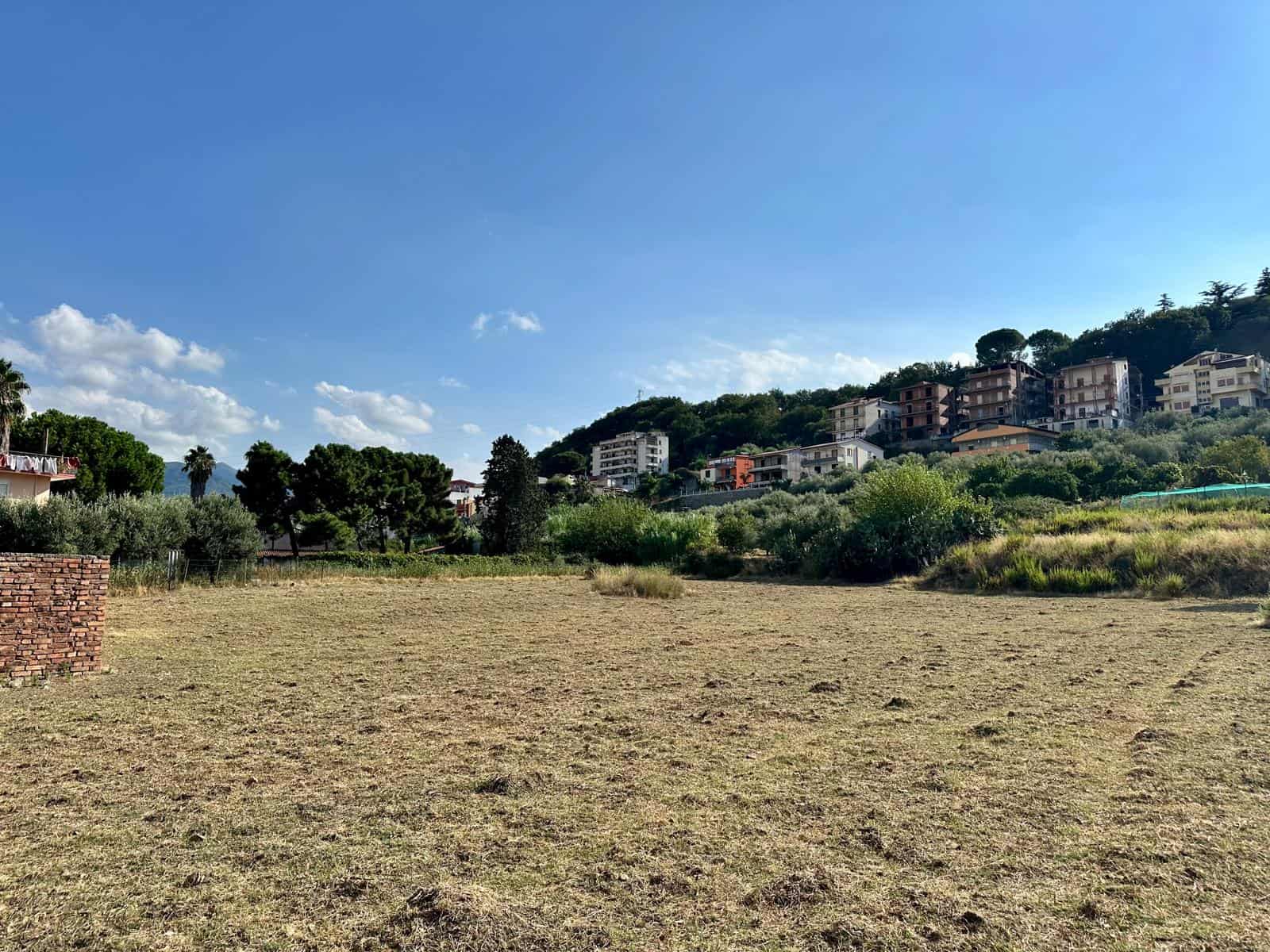 Prato di terreno edificabile con ville e residence su collina verde, cielo sereno, zona residenziale, natura, investimento immobiliare, panorama, prossimità al mare.