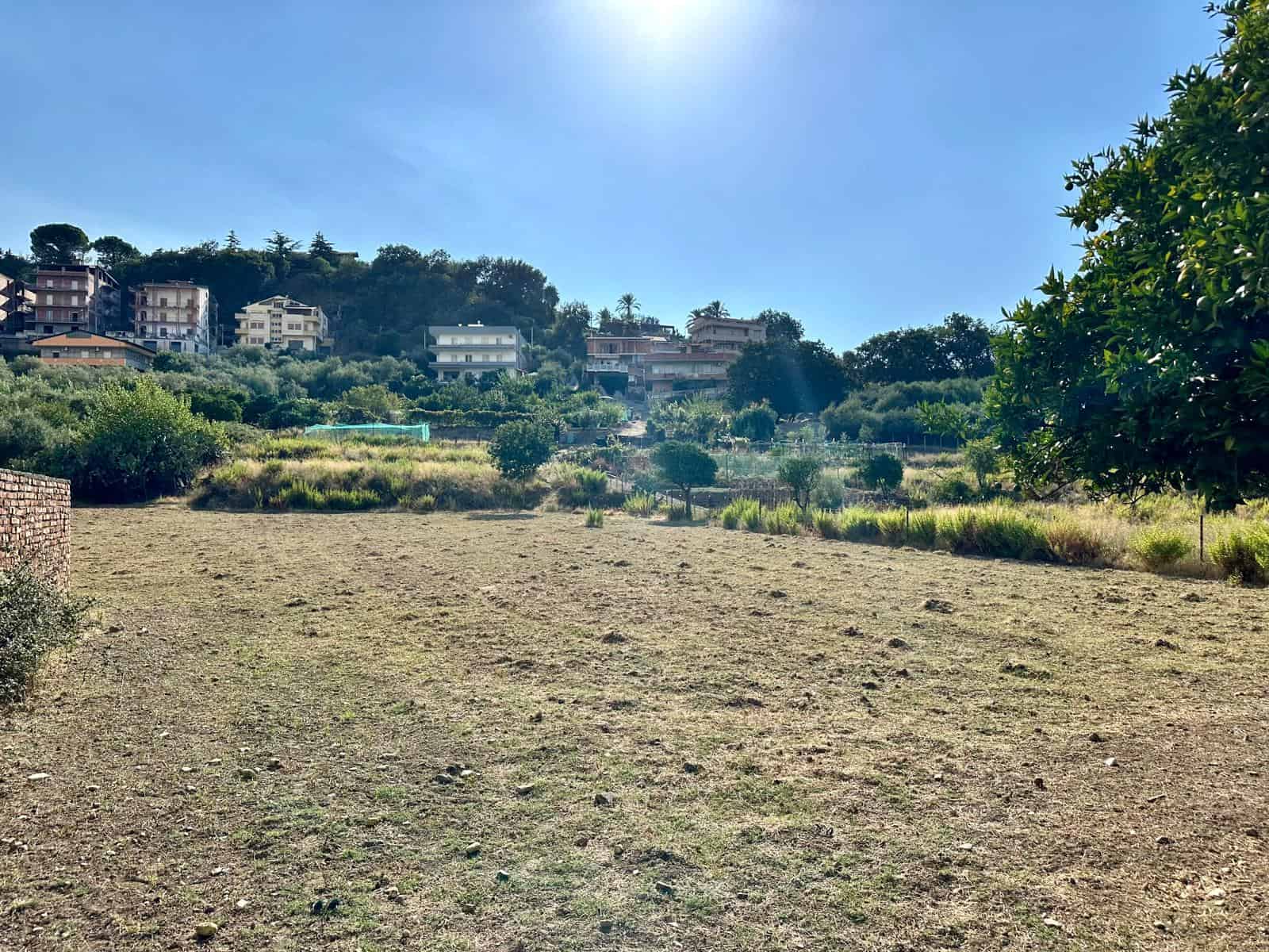 Campagna Toscana con case moderne sullo sfondo, paesaggio naturale e tranquillo, terreno aperto e soleggiato, ideale per costruzioni o orto, vista panoramica su colline e vegetazione, stile di vita outdoor, NextCasa.
