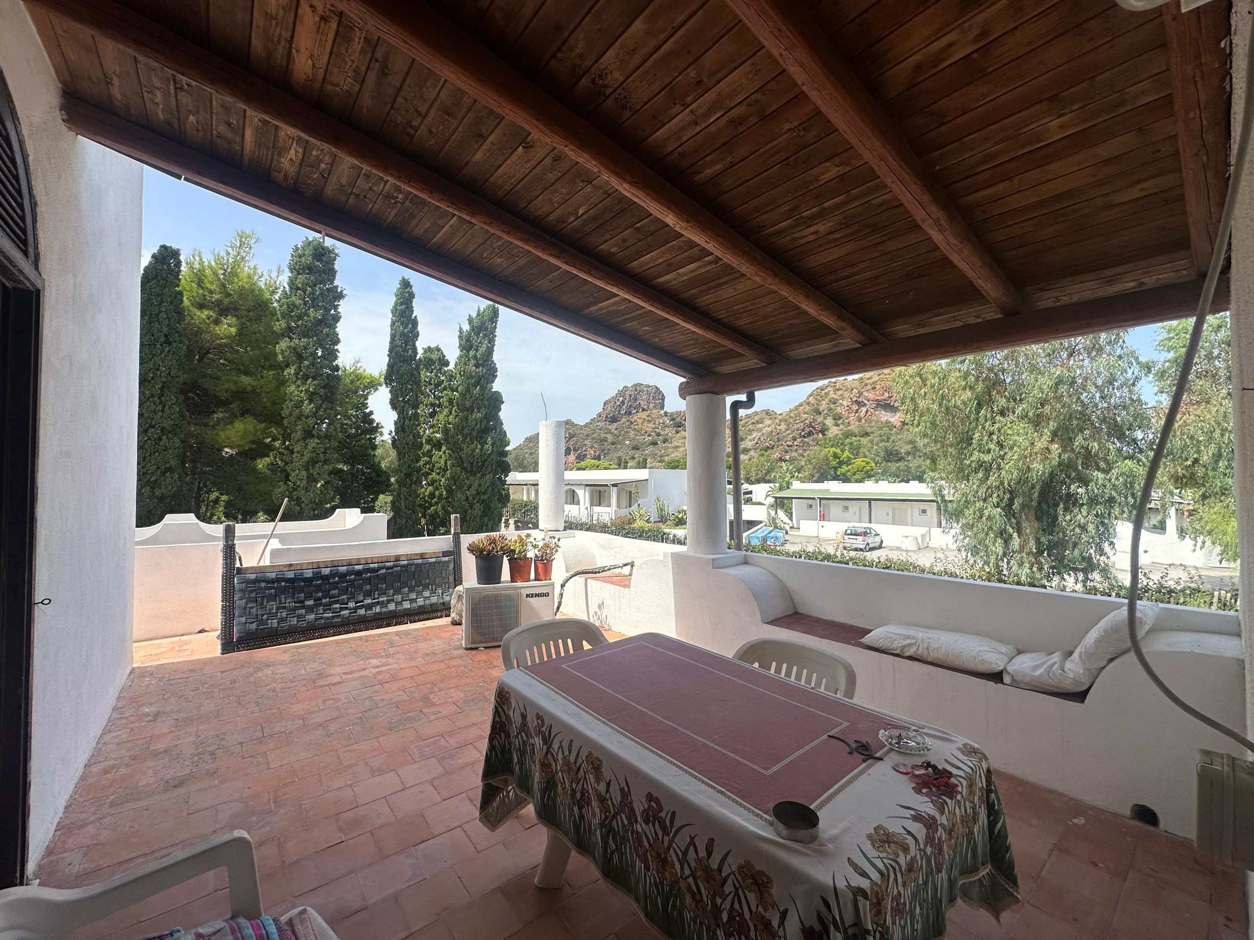 Balcone terrazzato con vista su natura, alberi e montagne, spazio esterno con tavolo e sedie, ideali per relax e cene all'aperto, stile mediterraneo, ambiente accogliente e luminosezone esterna NextCasa.