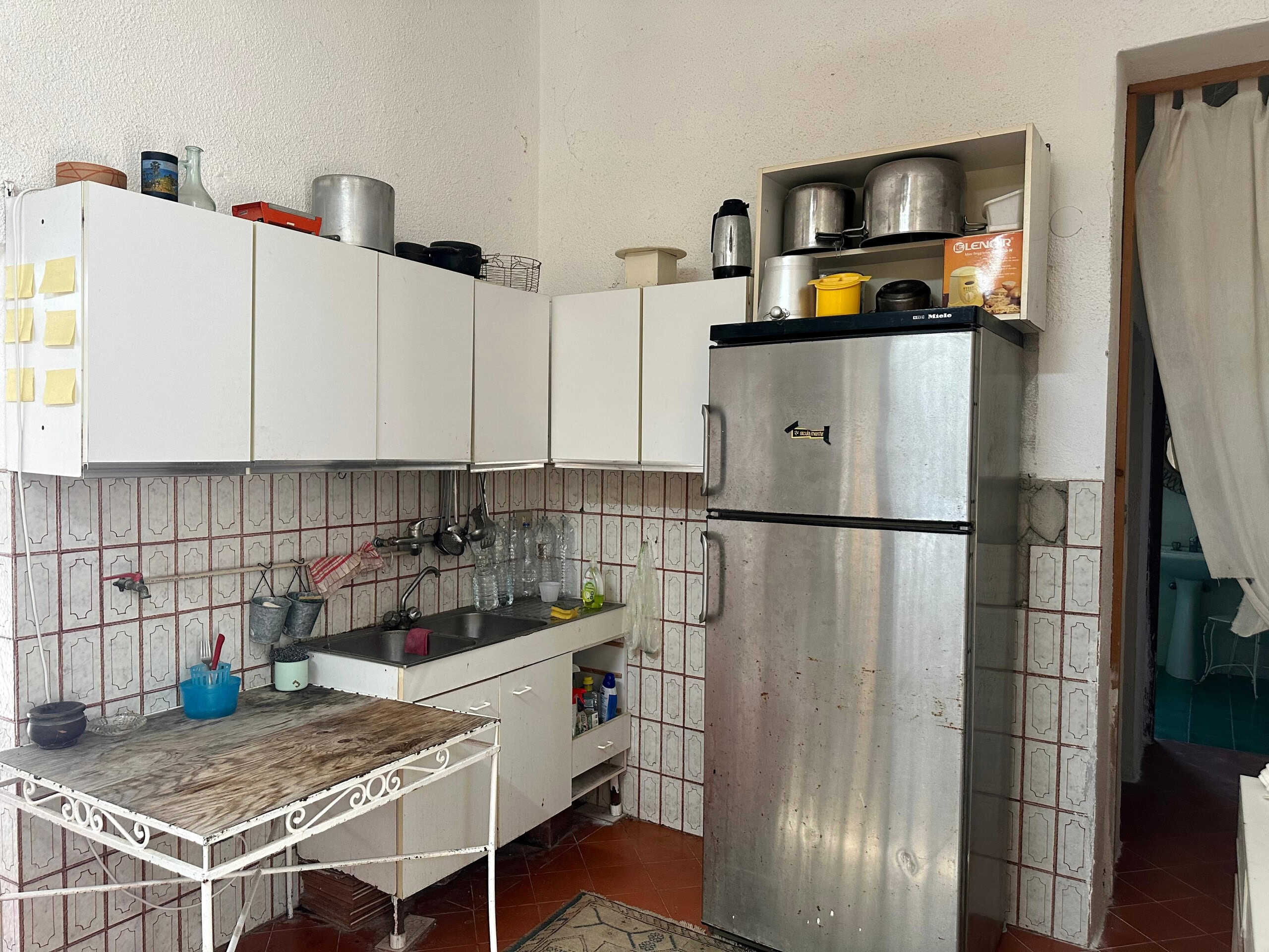 Fondo cucina con frigorifero frigo, pensili bianchi, lavabo e stoviglie, ambiente abitabile e funzionale.