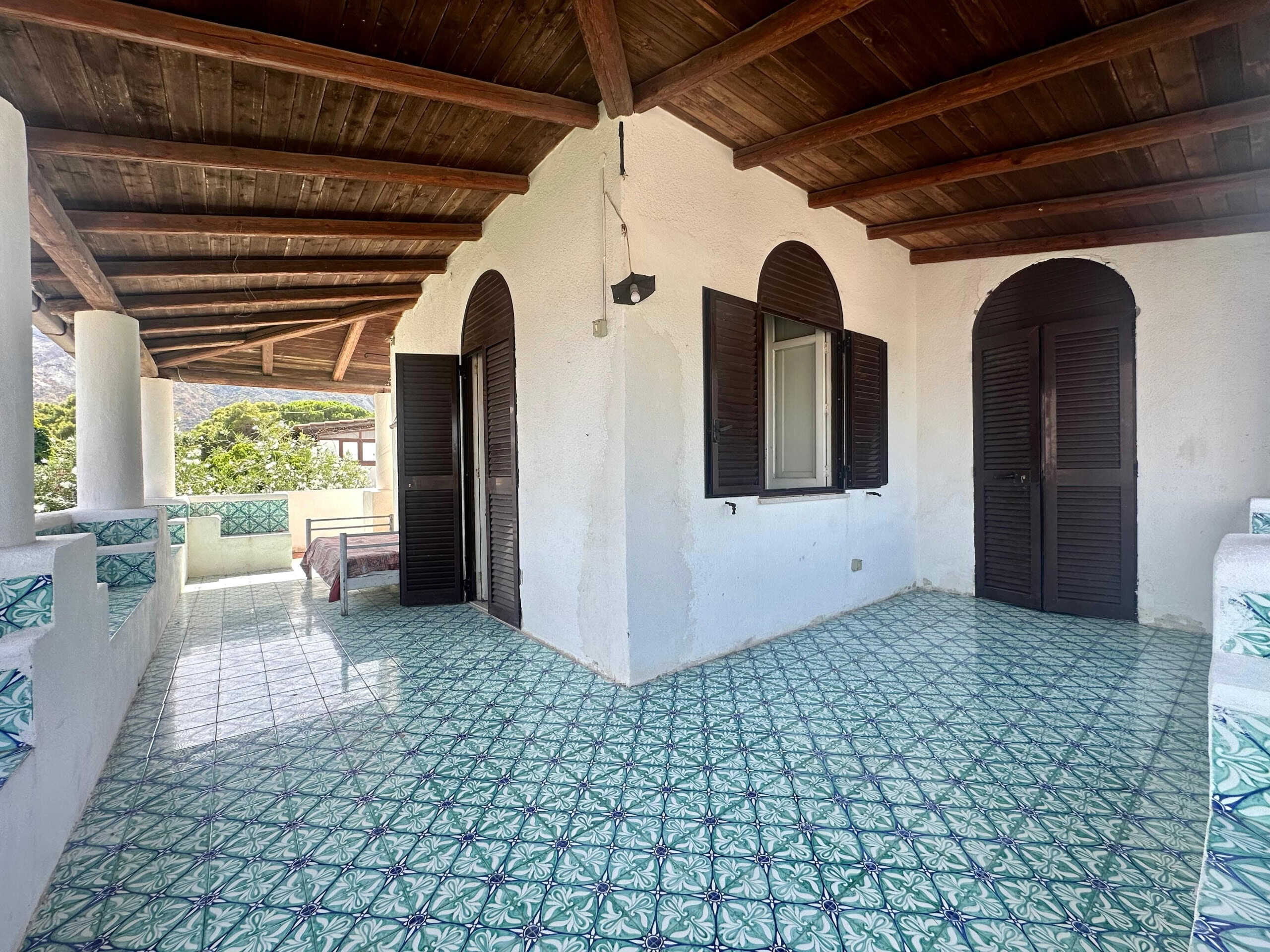 Balcone con terrazza in stile mediterraneo, pavimentato con piastrelle decorate, coperto da tetto in legno con travi a vista, ambiente esterno ideale per relax e convivialità.