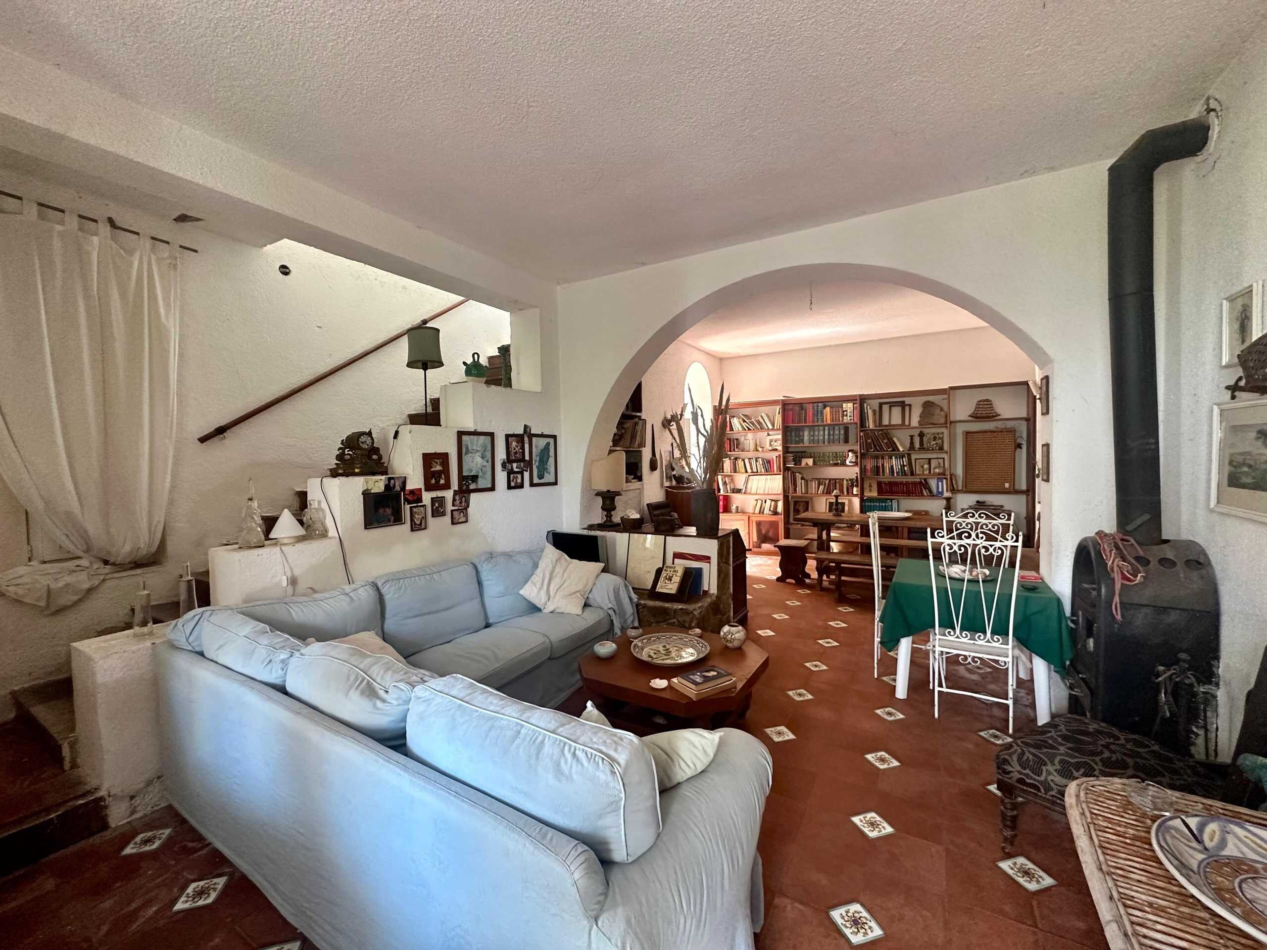 Ampio soggiorno con divani bianchi, libreria in legno, camino e decorazioni vintage in stile rustico. Pareti bianche, piastrelle con motivi floreali e arredi accoglienti creano un’atmosfera calda e familiare.