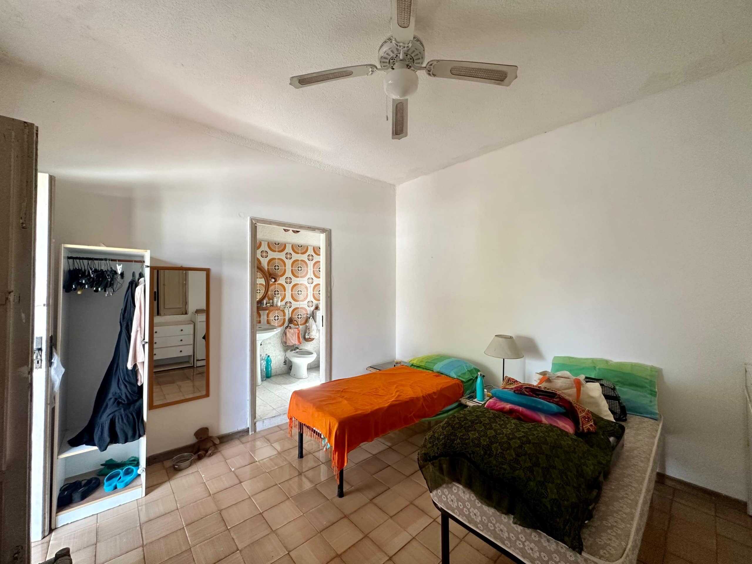 Letto singolo e matrimoniale in camera da letto con accessori, bagno visibile, pareti bianche, dettagli di arredamento semplice, illuminazione naturale, pavimento in piastrelle, stile basic e funzionale.