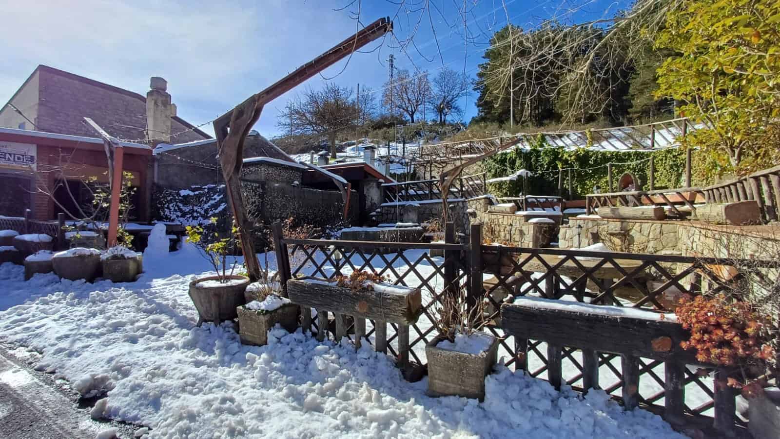 1. Splendido giardino invernale con piante e decorazioni in neve, vista panoramica su collina e struttura rustica, ideale per case vacanza e immobili in montagna.