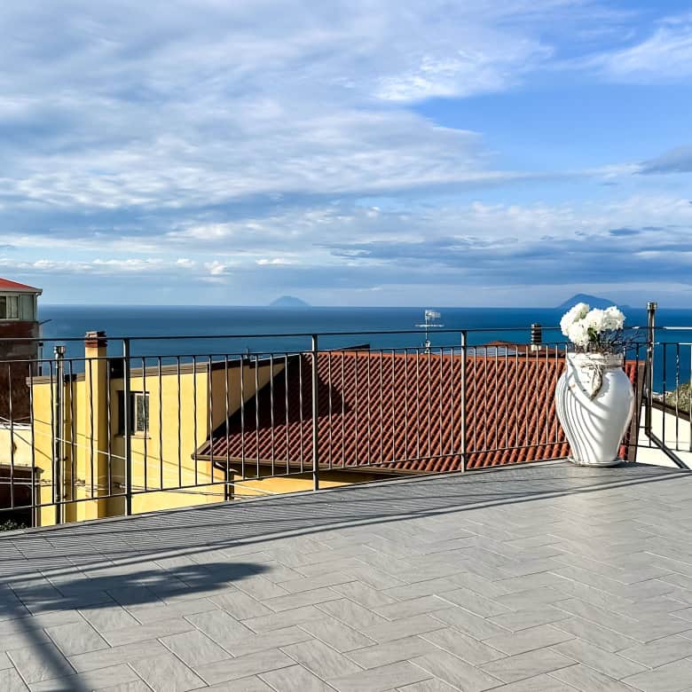 Vasto terrazzo con vista mare, case con tetti rossi, cielo nuvoloso, dettagli architettonici, ideale per immobiliare e design abitativo.