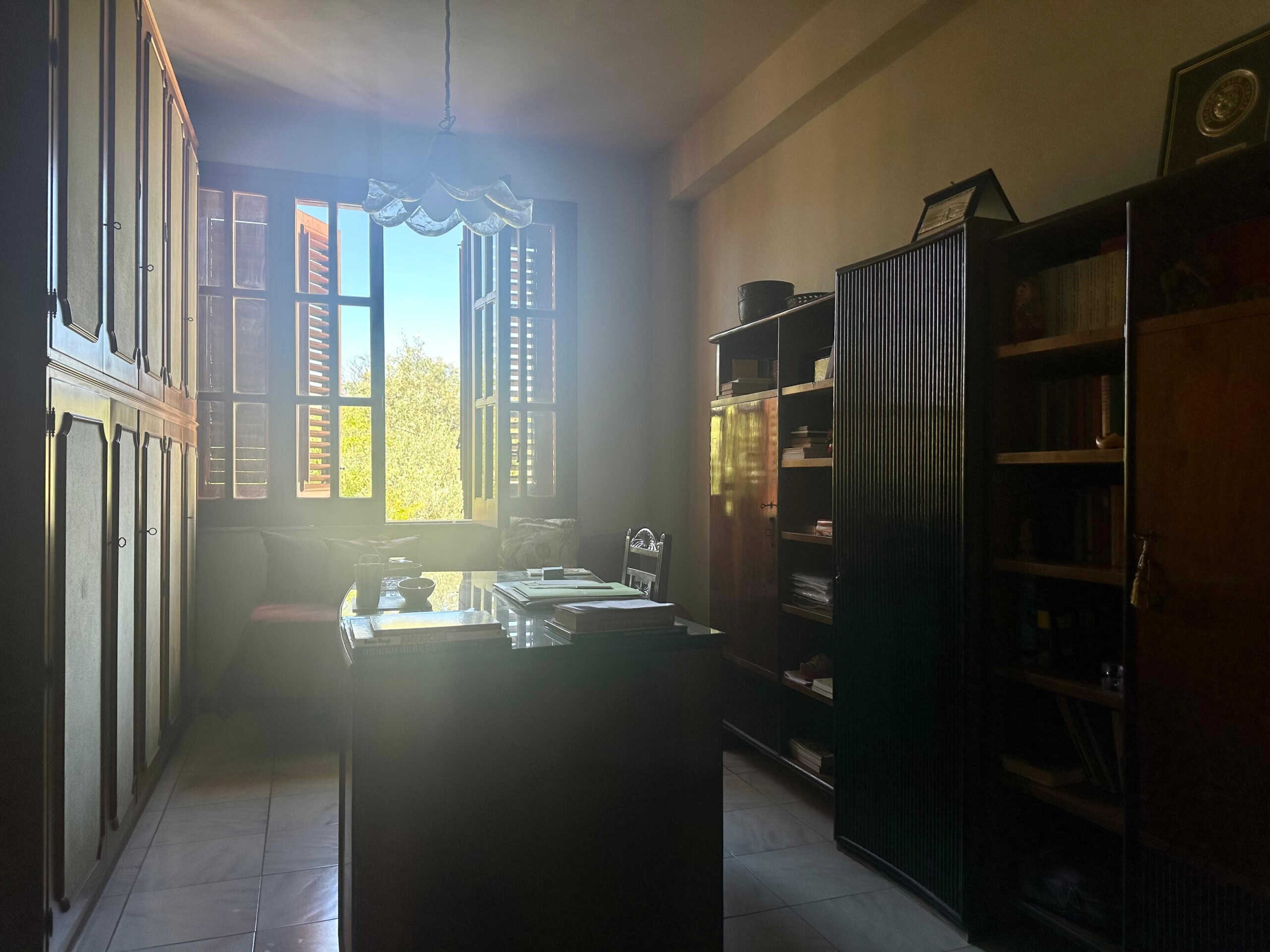 Armadio a muro e librerie in soggiorno con finestra aperta, luce naturale, ambiente classico, mobili in legno scuro, stanza luminosa e accogliente, stile tradizionale.
