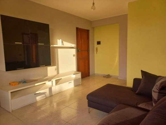 Spazioso soggiorno arredato con divano marrone e mobile TV bianco, parete gialla, porta d'ingresso in legno, illuminazione naturale, ambienti eleganti e accoglienti, ideale per vivere confortevoli momenti.