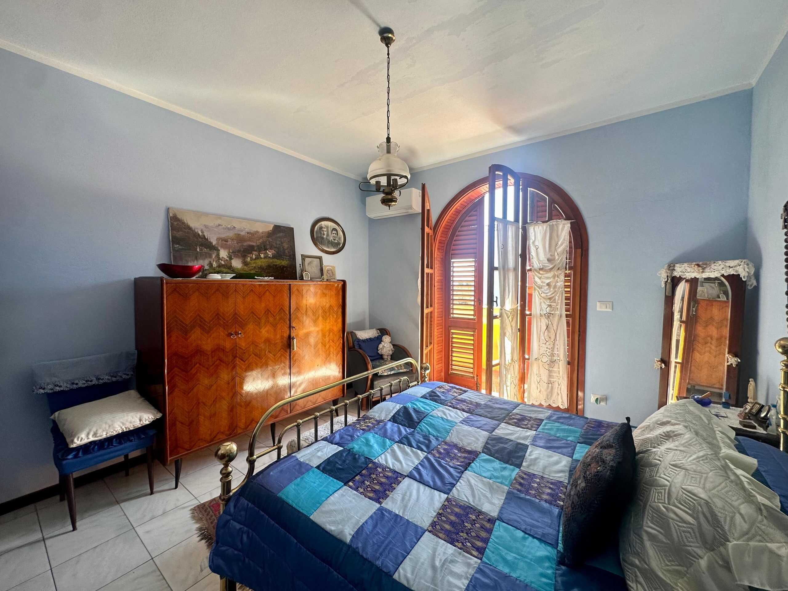Armadio in legno vintage, stanza da letto luminosa con letto in ferro battuto, balcone con persiane in legno, decorazioni classiche, ambiente accogliente e spazioso in stile tradizionale italiana, NextCasa.