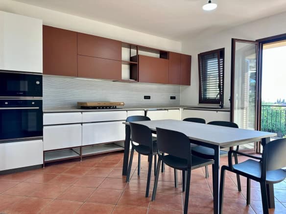 Cucina moderna con mobili bianchi e armadi marroni, spazio luminoso con finestra aperta, ideale per soggiorni di design e convivialità.