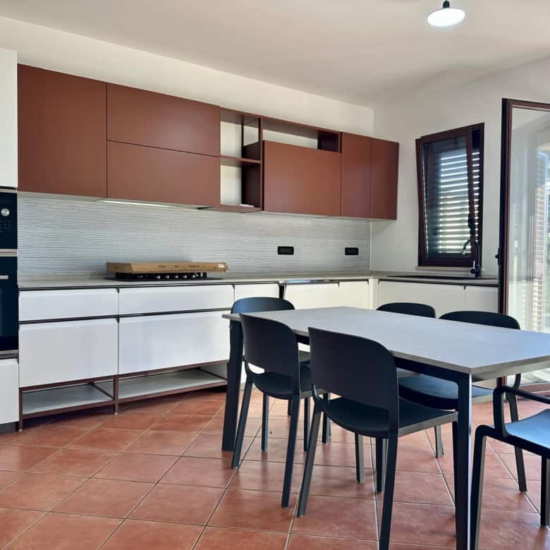 Cucina moderna con mobili bianchi e armadi marroni, spazio luminoso con finestra aperta, ideale per soggiorni di design e convivialità.
