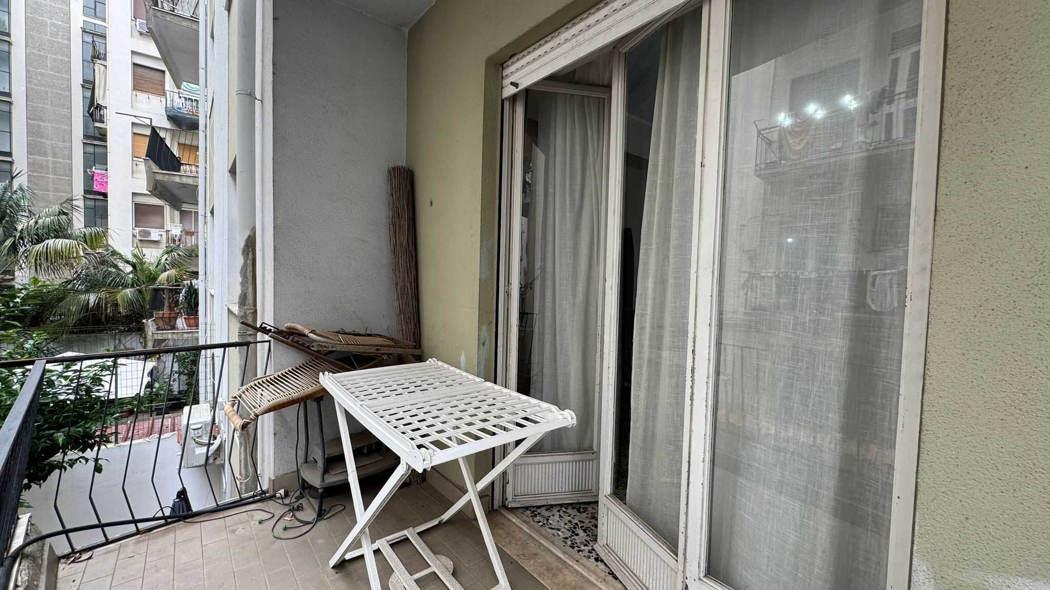 Balcone con accesso a un appartamento, con stendibiancheria, sedie impagliate e vista su altri condomini in città. Ideale per relax e linea di vita quotidiana.