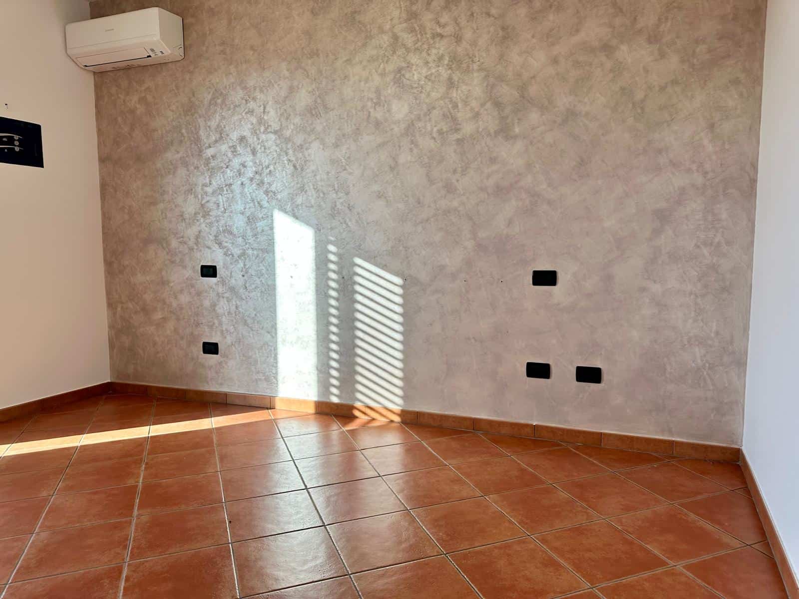 Ampio spazio vuoto in una stanza moderna con pareti in tonalità neutra, pavimento in piastrelle di terracotta e aria condizionata, ideale per residenze o uffici.