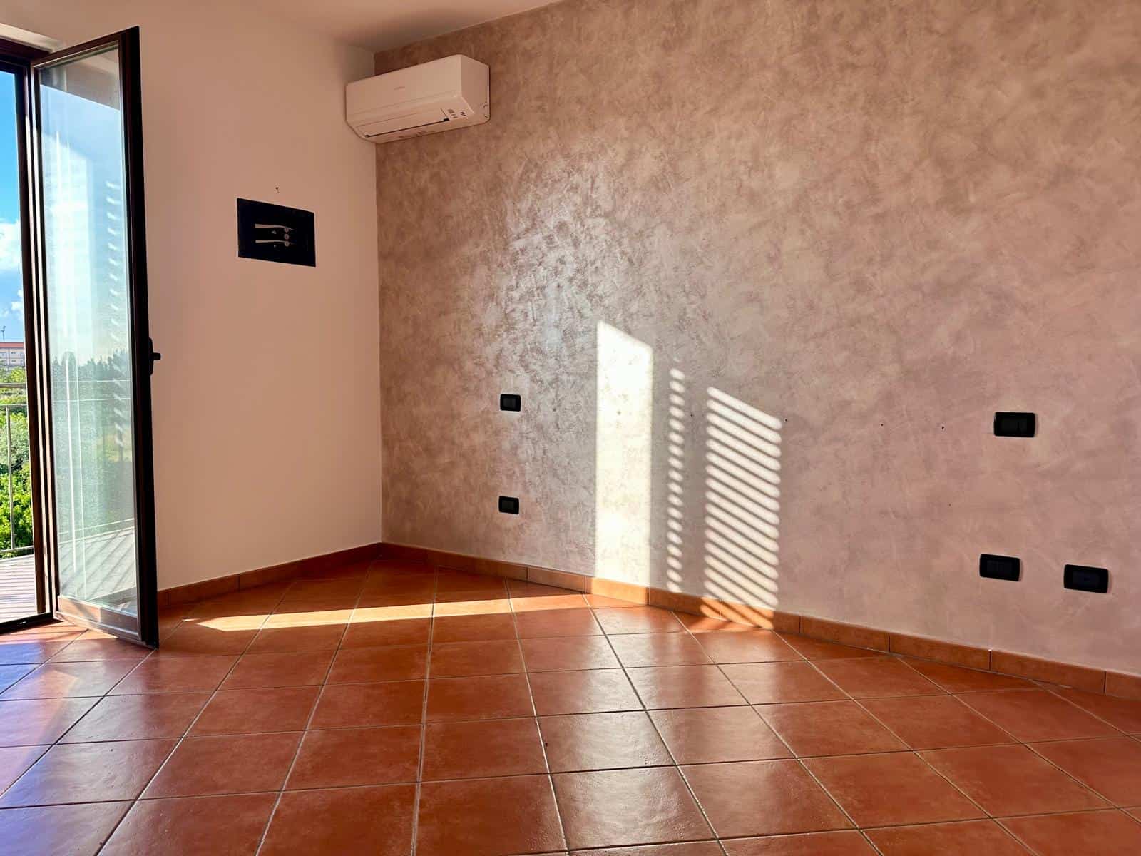 Ampio soggiorno con parete decorativa e aria condizionata, luminoso grazie alla porta finestra che dà sul balcone, pavimento in piastrelle di terracotta, ideale per ambienti moderni e accoglienti.