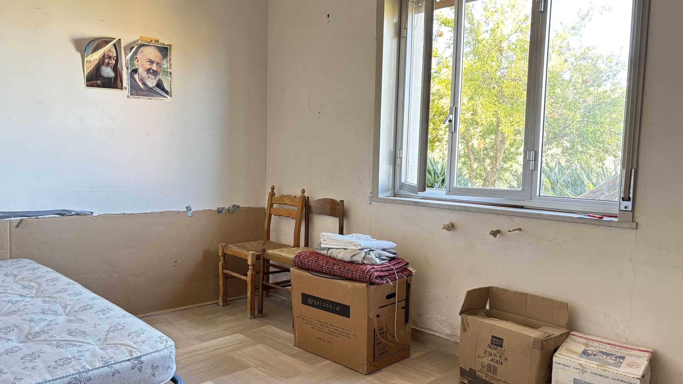 Nuova casa in fase di ristrutturazione con pareti da tinteggiare e arredi ancora da sistemare, luce naturale proveniente dalla finestra, ambiente accogliente e in trasformazione.