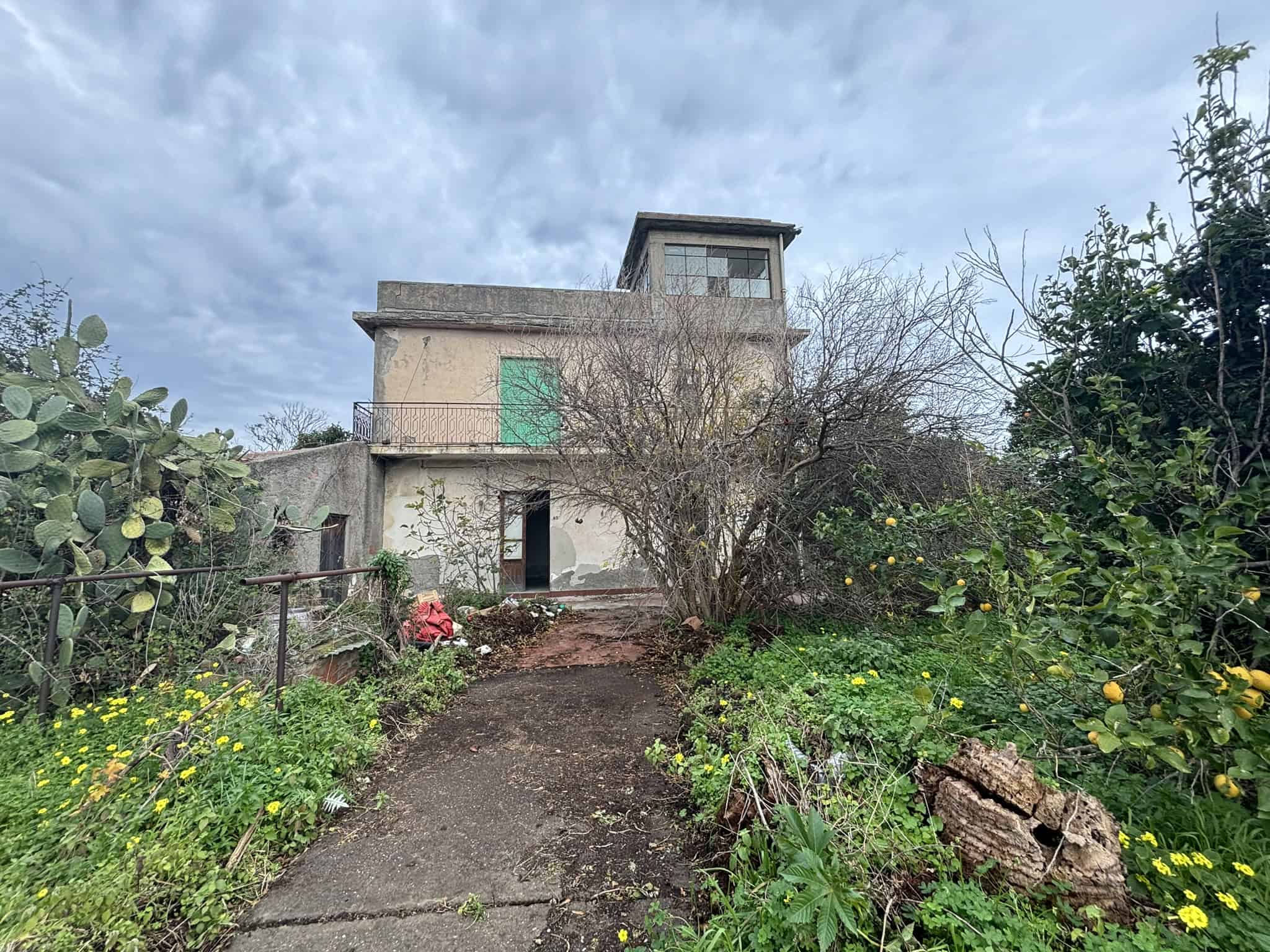 Casa da ristrutturare con giardino, vista su cielo nuvoloso, edificio a più piani con terrazza e piante rigogliose, in zona residenziale, opportunità immobiliare, NextCasa.