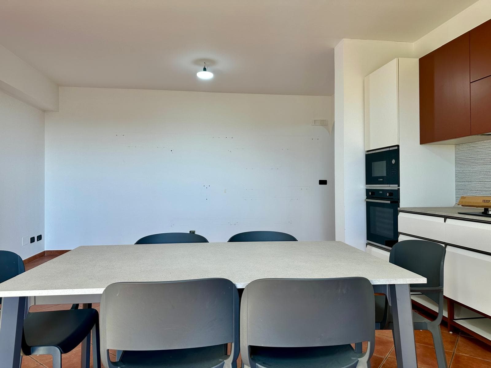 Interno di una cucina moderna con tavolo da pranzo e sedie, pareti bianche e armadi in legno, ideale per appartamenti in affitto o vendita a NextCasa.