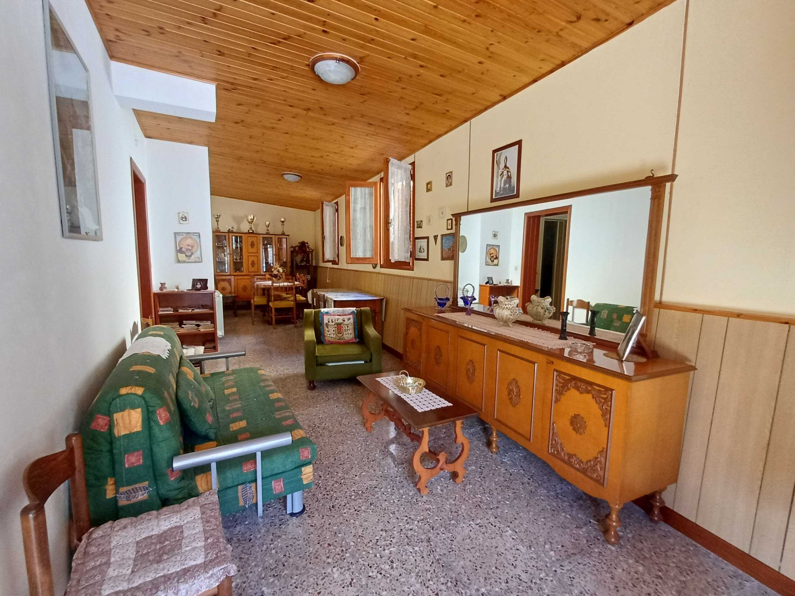 Ampia sala soggiorno con mobili vintage e pareti decorate, pareti in legno e soffitto spiovente, ideale per case residenziali e ambienti familiari.