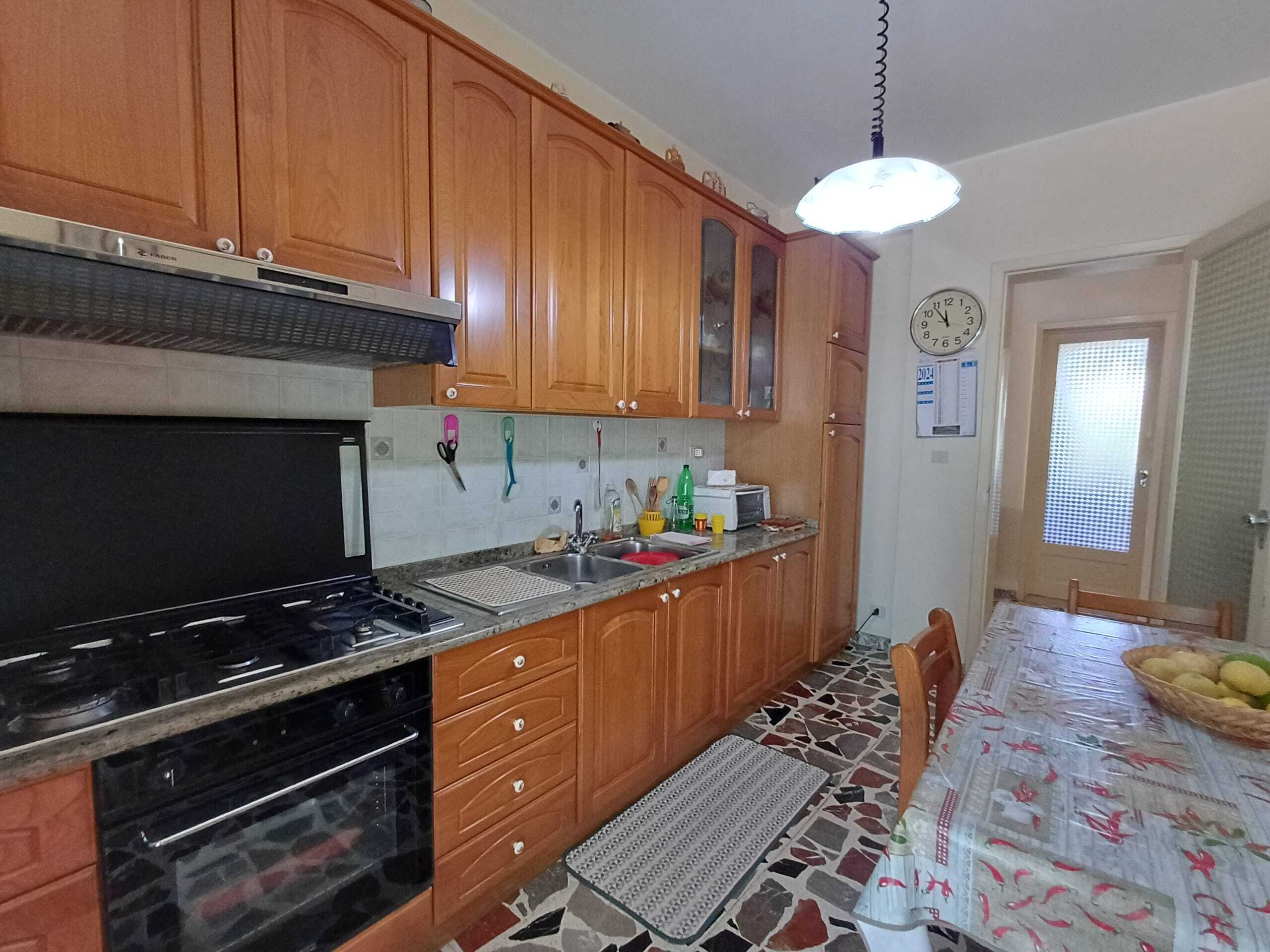 Cucina abitabile con mobili in legno, piano cottura a gas, forno e zona pranzo, immerse in un ambiente luminoso con pavimento in pietra e accessori pratici, ideale per living comfort.