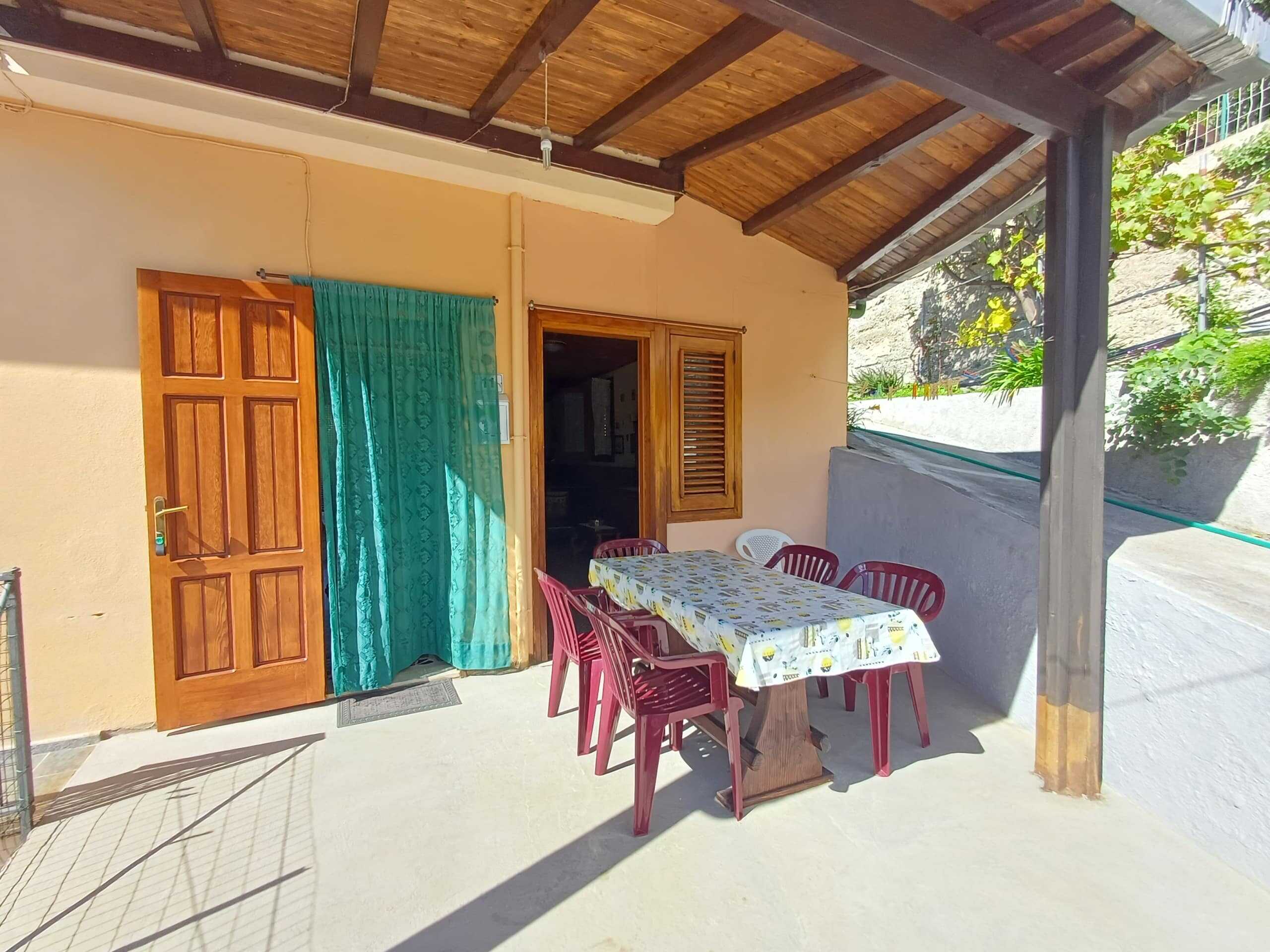 Vista esterna di una terrazza con tavolo e sedie in ambiente domestico, ideale per mangiare all'aperto in un contesto di casa vacanze NextCasa, con pareti gialle, serramenti in legno e copertura in legno.