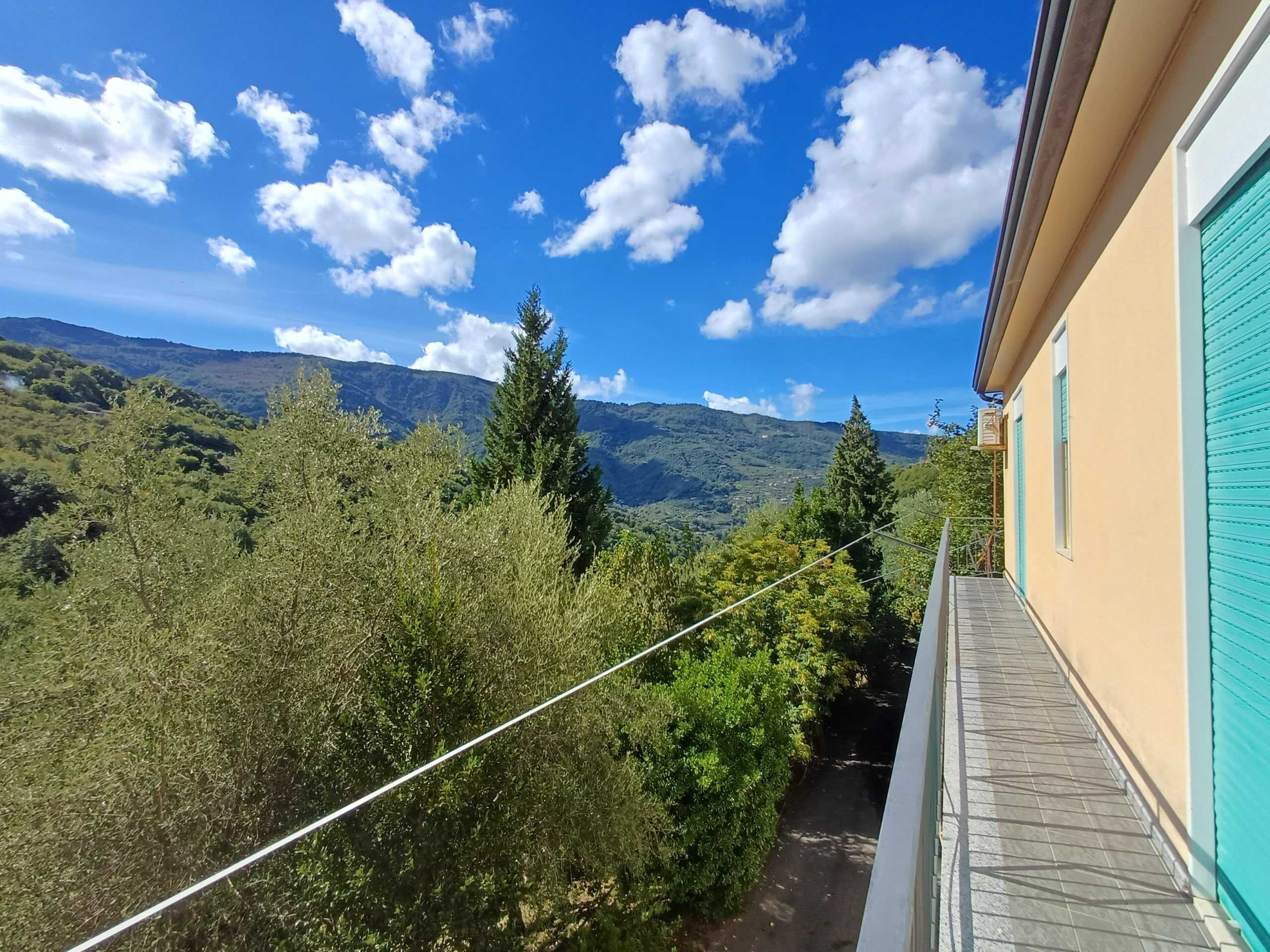 Vista panoramica delle montagne e del cielo azzurro dal balcone di una casa in campagna, immersa nella natura con alberi verdi e un paesaggio suggestivo, ideale per acquisto e affitti immobili.