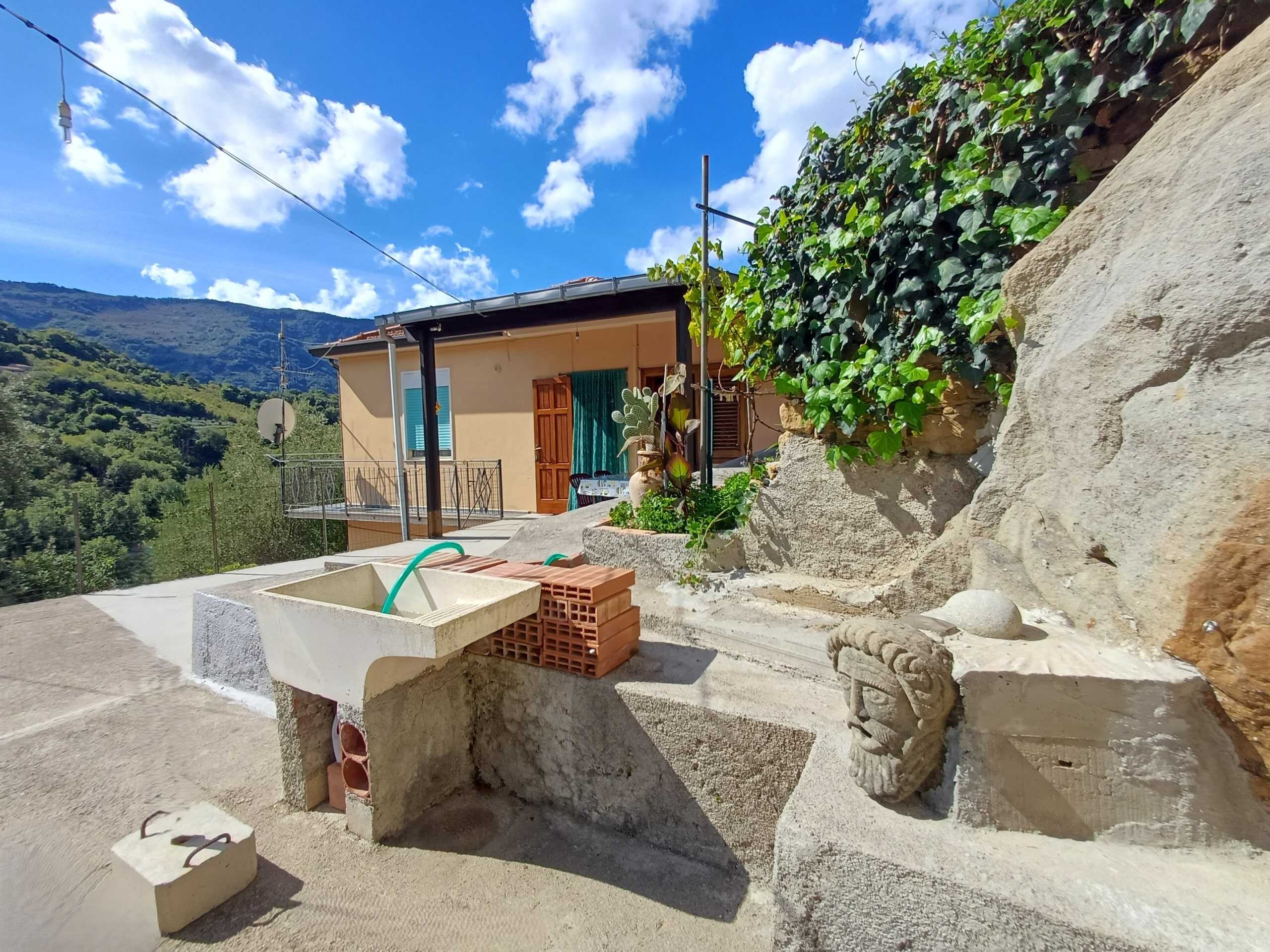 Scorcio di terrazza con lavandino in pietra e decorazioni artistiche, vista sulle colline verdi e cielo azzurro, ideale per relax e momenti all'aperto in una casa in campagna.