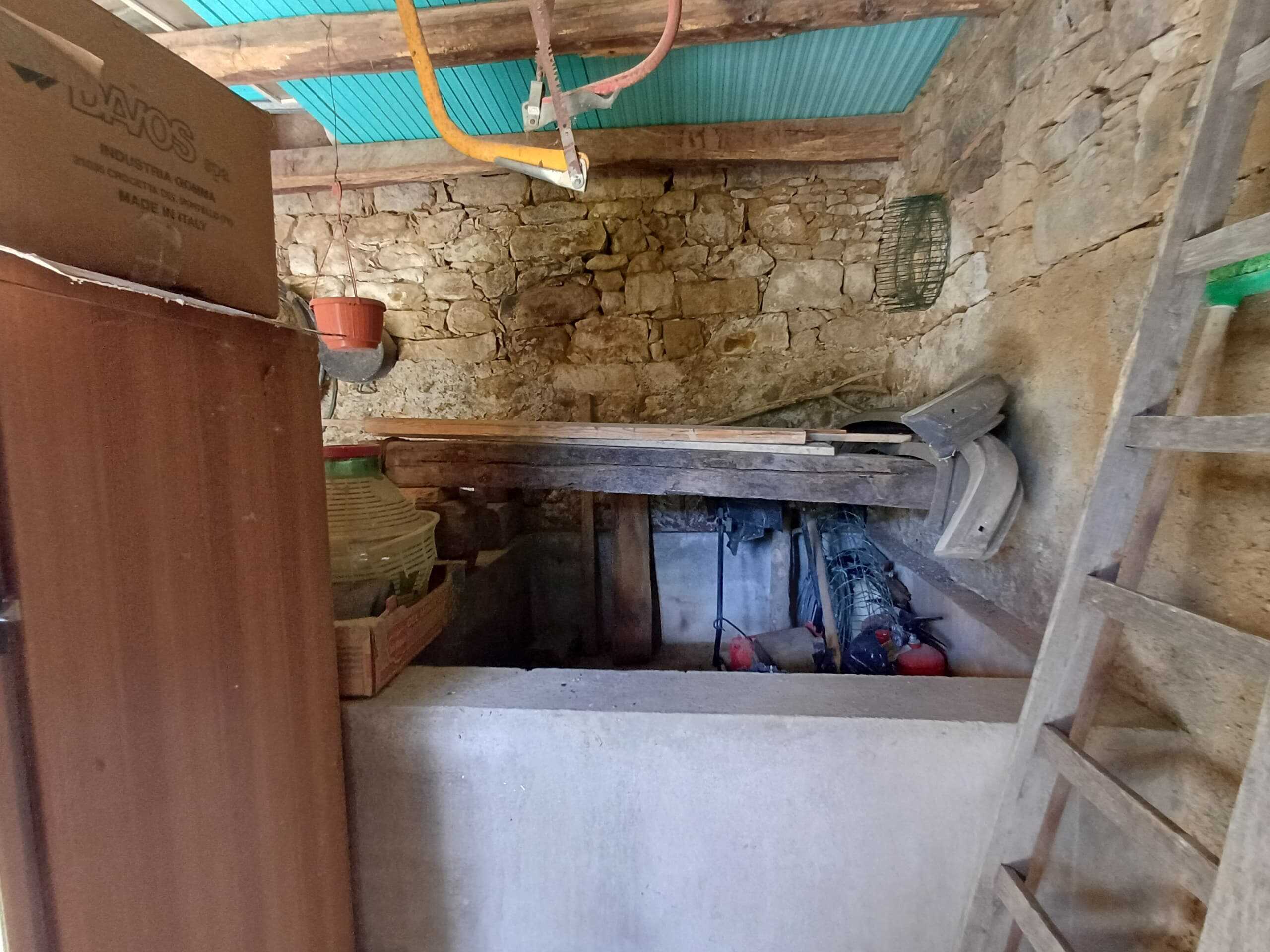 Ripostiglio rustico con pareti in pietra e soffitto in legno, attrezzi da giardinaggio e scaffalature in legno, adatto per il deposito e la conservazione di attrezzi e materiali da bricolage.