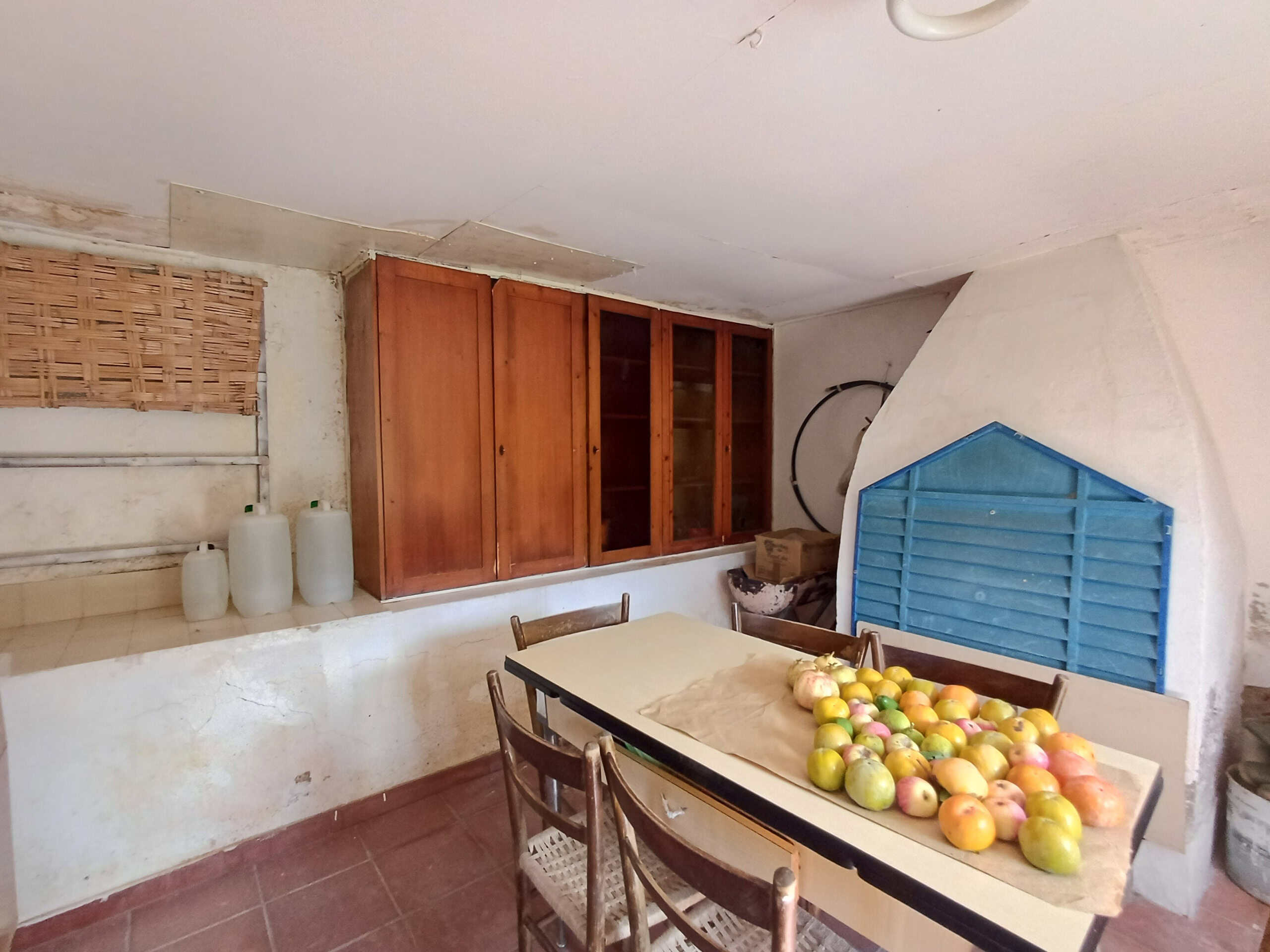 Pianeta casalingo rustico con tavolo, sedie, mazzo di mele sulla superficie, armadietto in legno, mattoni, contenitori d'acqua, ambientazione campestre, atmosfera rustica e accogliente.