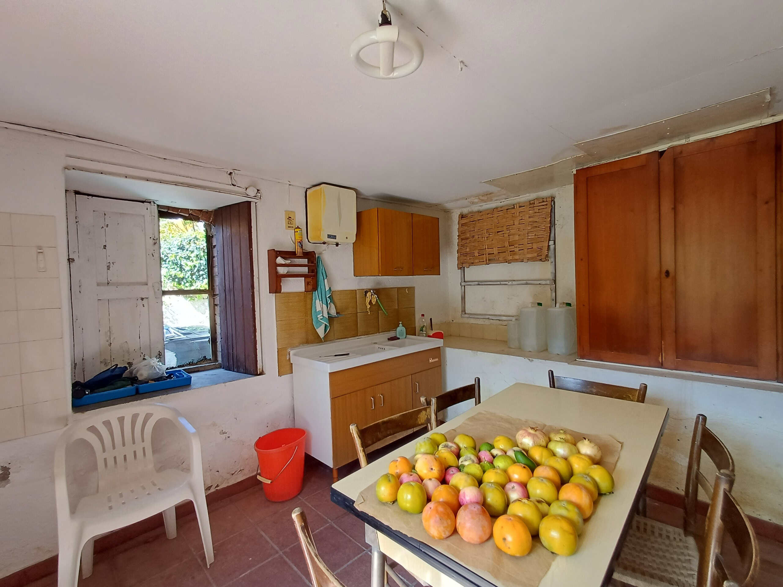 Vecchia cucina rustica con tavolo e frutta, ambientazione domestica, mobili in legno, finestra vecchia, atmosfera tradizionale e semplice, casa di campagna o rustico, dettagli vissuti.