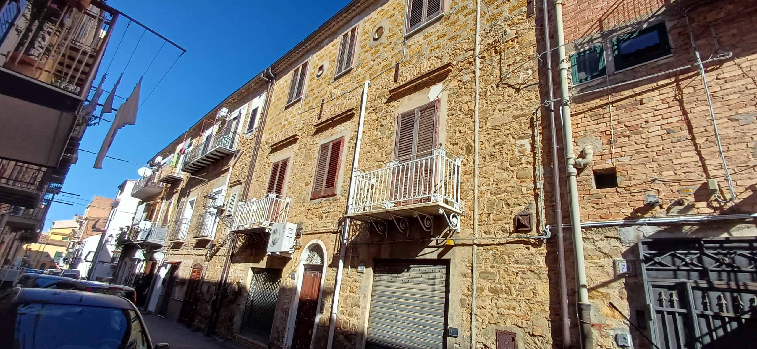 Vecchia casa in pietra con balconi in ferro battuto e finestre con ante di legno, inquartiere storico di città italiana, con appartamenti abitati e lavatrici stese per il bucato.