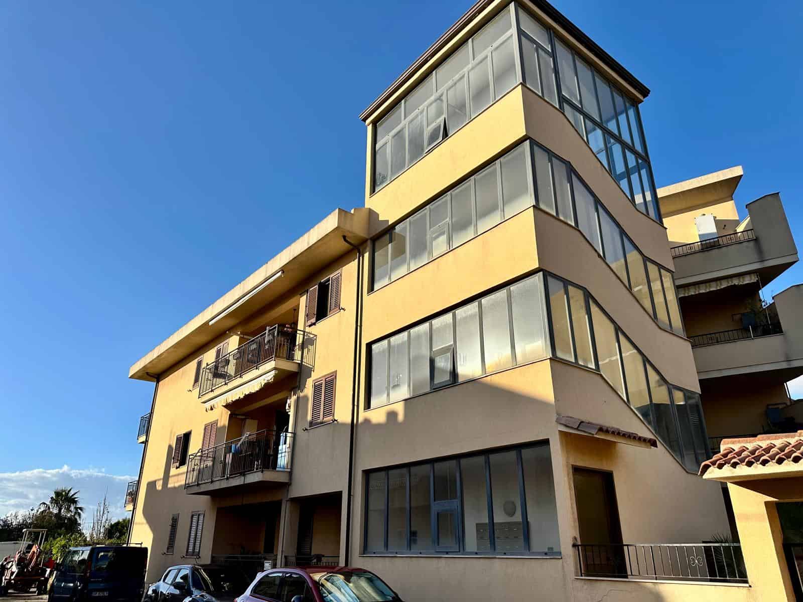 Balcone e facciata di un edificio residenziale moderno con ampie finestre e balconi, in un contesto urbano soleggiato, ideale per appartamenti di alta qualità e investimento immobiliare a NextCasa.