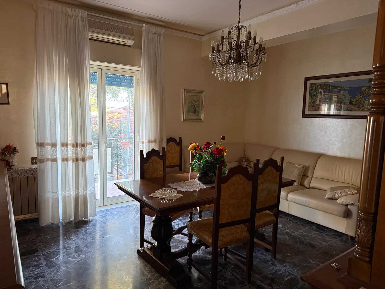 Elegantemente arredata sala da pranzo con mobili in stile classico, lampadario in cristallo, tende bianche e veranda luminoso con vista su giardino, ideale per vivere comfort e raffinatezza.