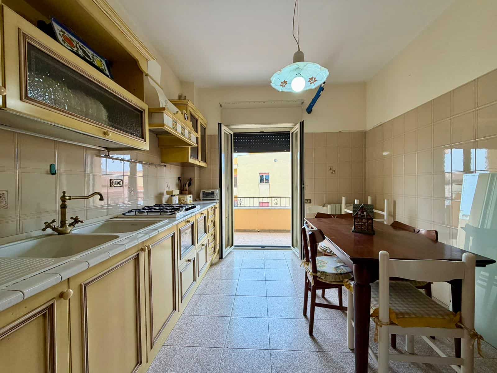 Ampio soggiorno con cucina abitabile, balcone e zona pranzo, arredamento classico, illuminazione naturale, pavimento in piastrelle chiare, ideale per famiglie e conviviale.