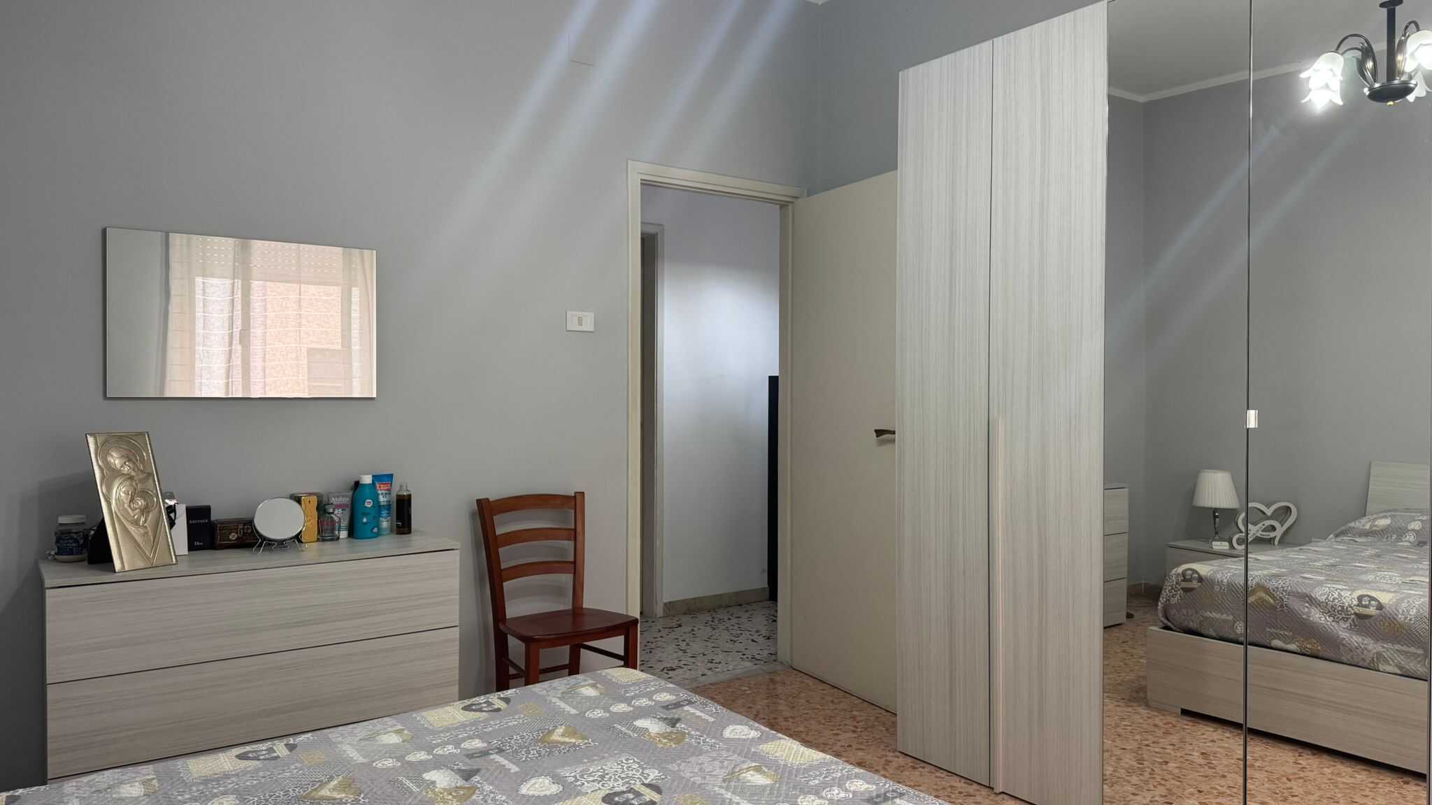 Armadio in camera con specchio, letto matrimoniale e mobile con oggetti personali, arredamento casa NextCasa, interni moderni e funzionali, ideale per soluzioni di arredamento italiane.