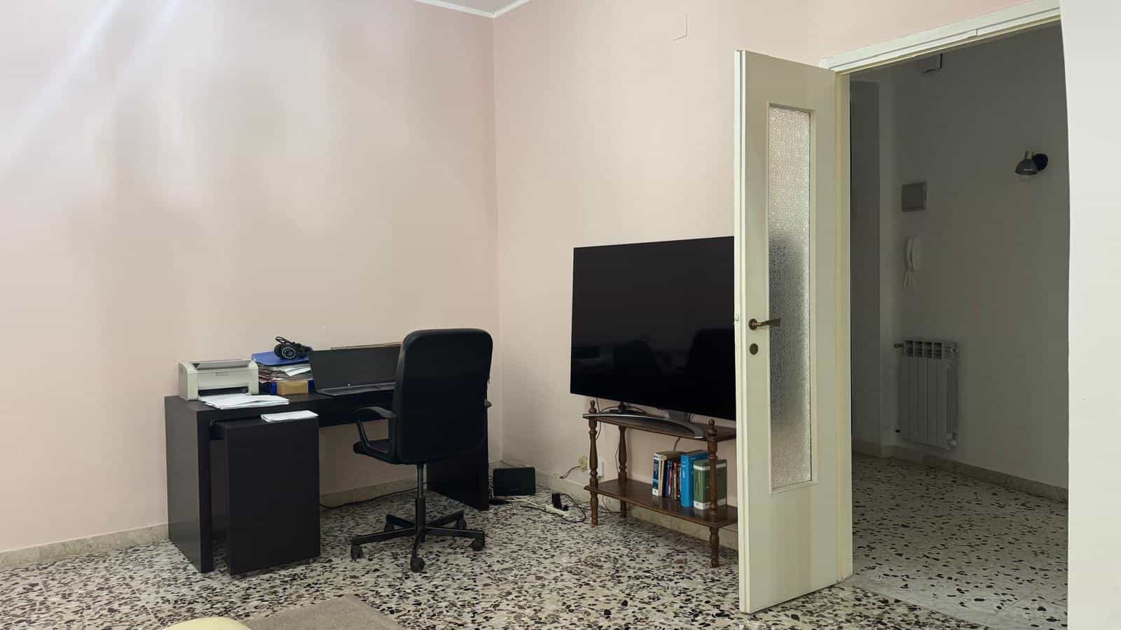 Scrivania da ufficio con computer e televisore in soggiorno, spazio funzionale e confortevole, ideale per lavoro o relax, con arredi pratici e uno stile semplice.