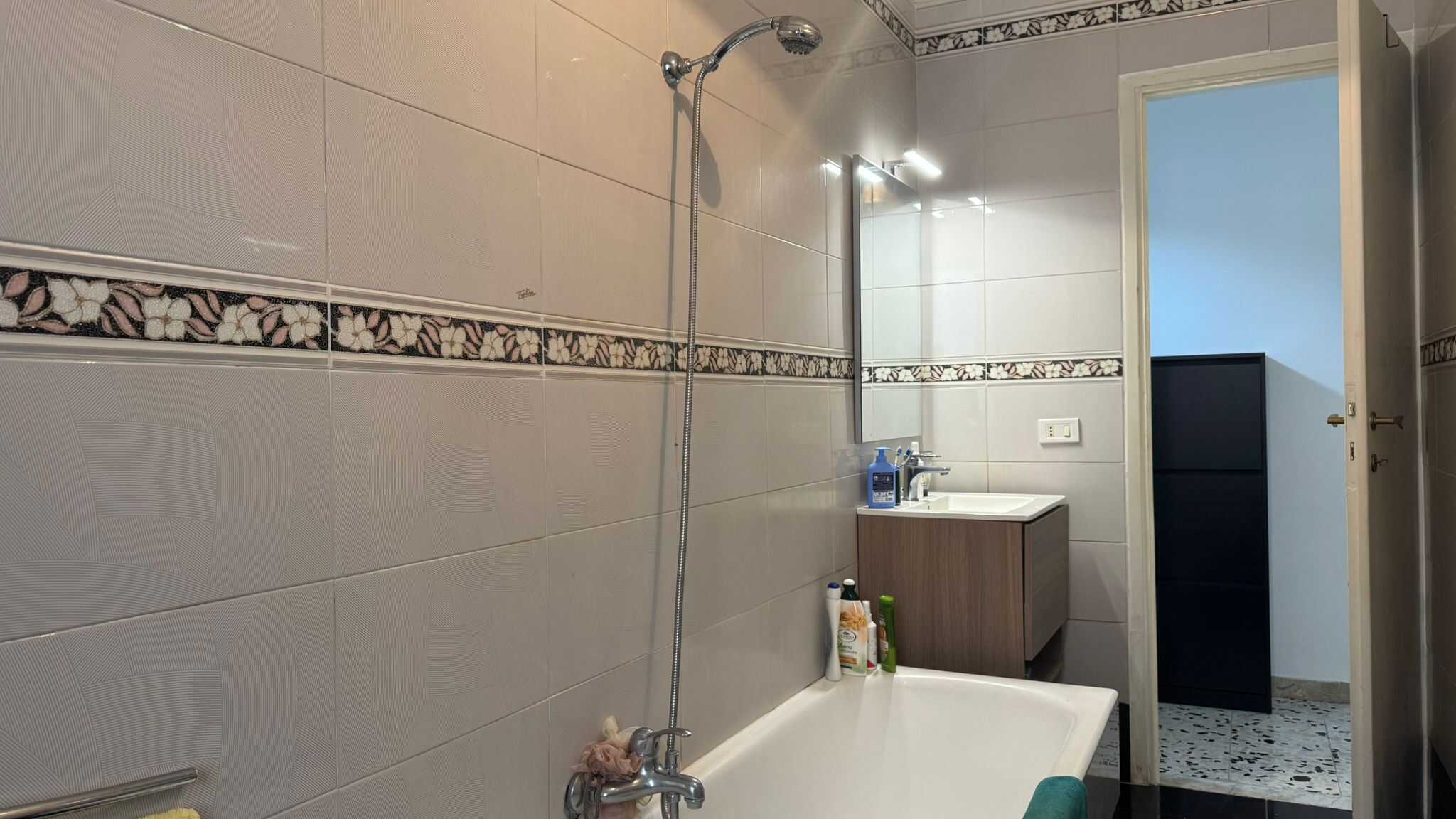 Lavabo e doccia nel bagno di una casa trifamiliare a Verano Brianza, arredato in stile semplice e funzionale, con accessori per la cura della persona e una parete in piastrelle chiare.
