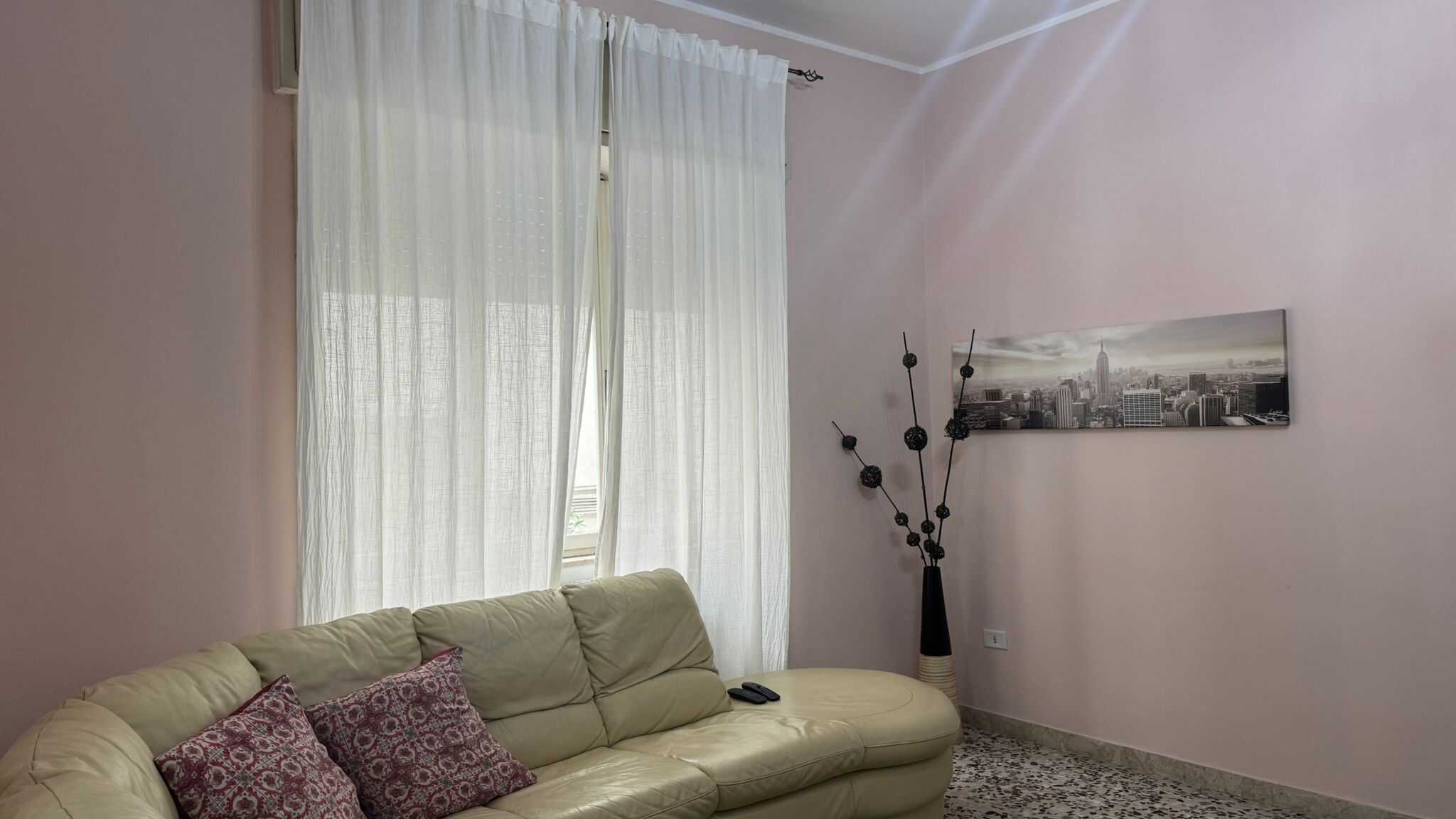 Soggiorno luminoso con divano beige, tende bianche e decorazioni moderne, ideale per ambienti residenziali eleganti e confortevoli.