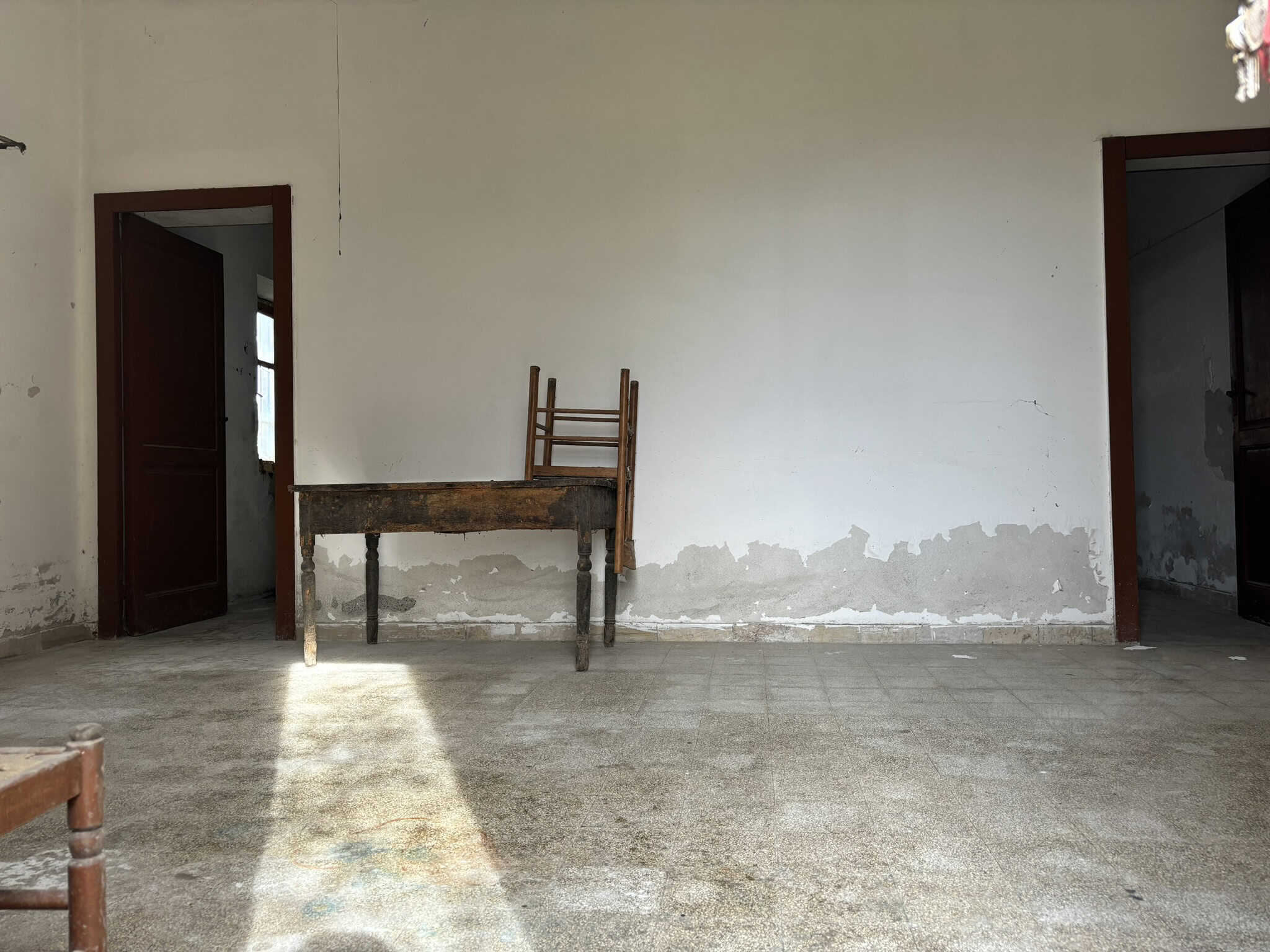 Vecchia parete di una stanza da ristrutturare, con presenza di mobili di legno e pavimento in piastrelle usurate, che evidenzia l'occasione di restauro e rinnovamento immobiliare per l'interiore di casa.